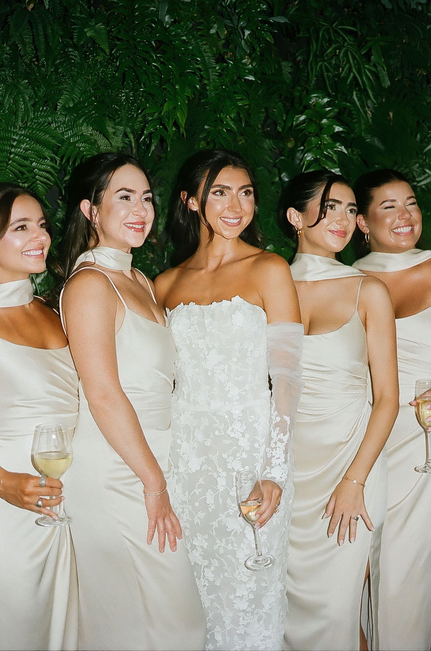 Bridesmaids in champagne dresses line up with the bride in white for a formal wedding photo.