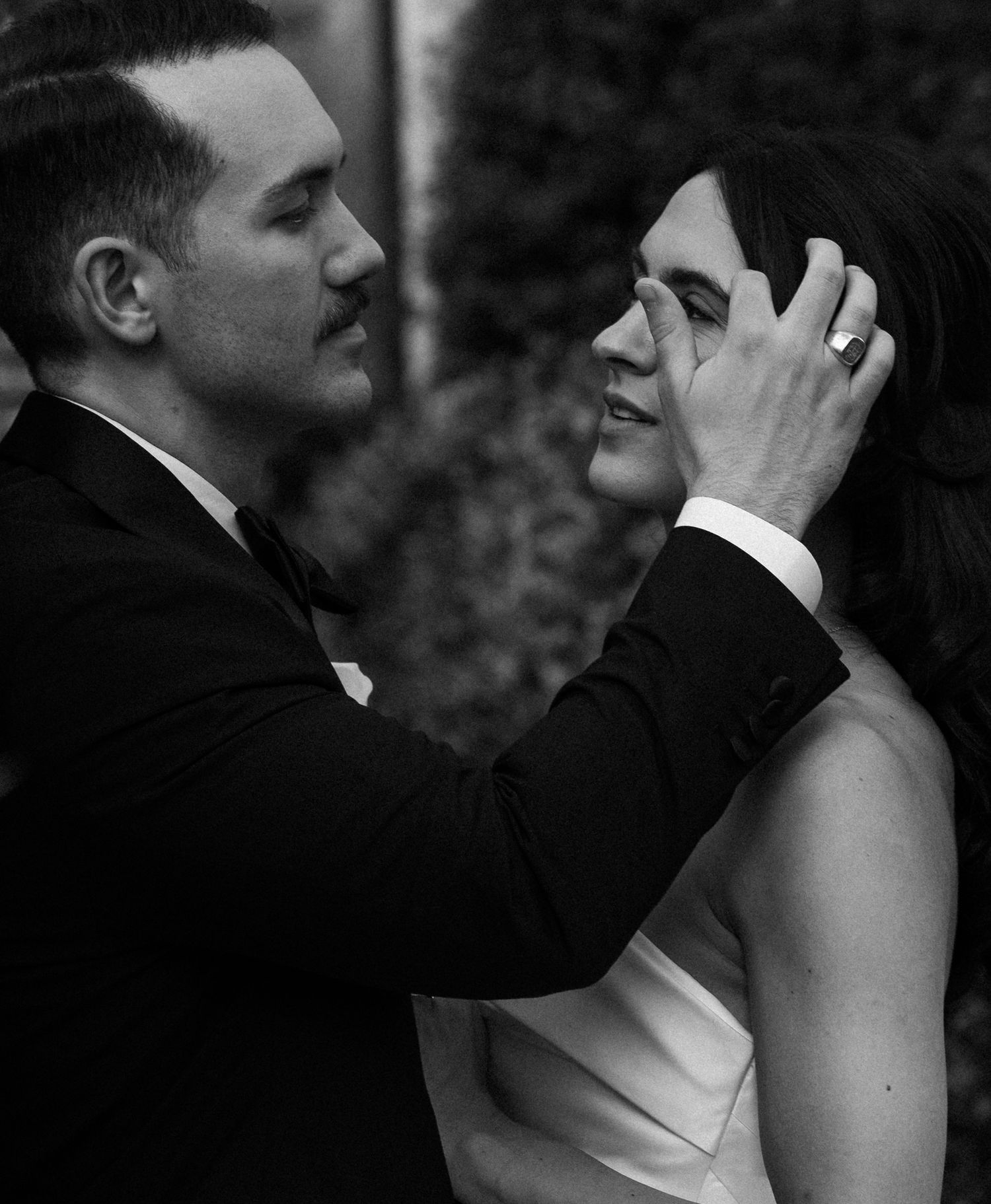 Black and white photo of a groom tenderly cupping his smiling bride's face during their wedding day.