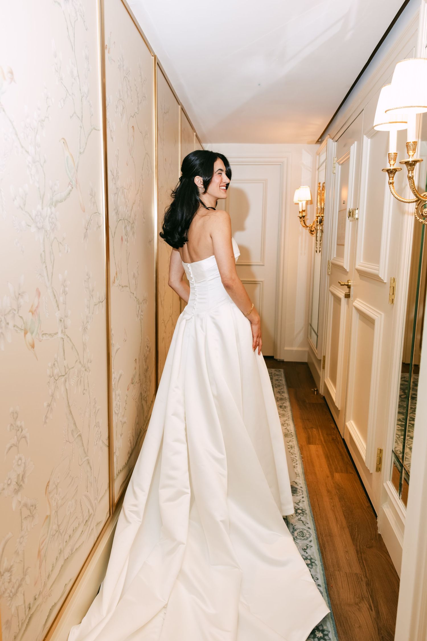 Elegant bride in strapless white satin ball gown with long train standing in a luxurious hotel corridor.