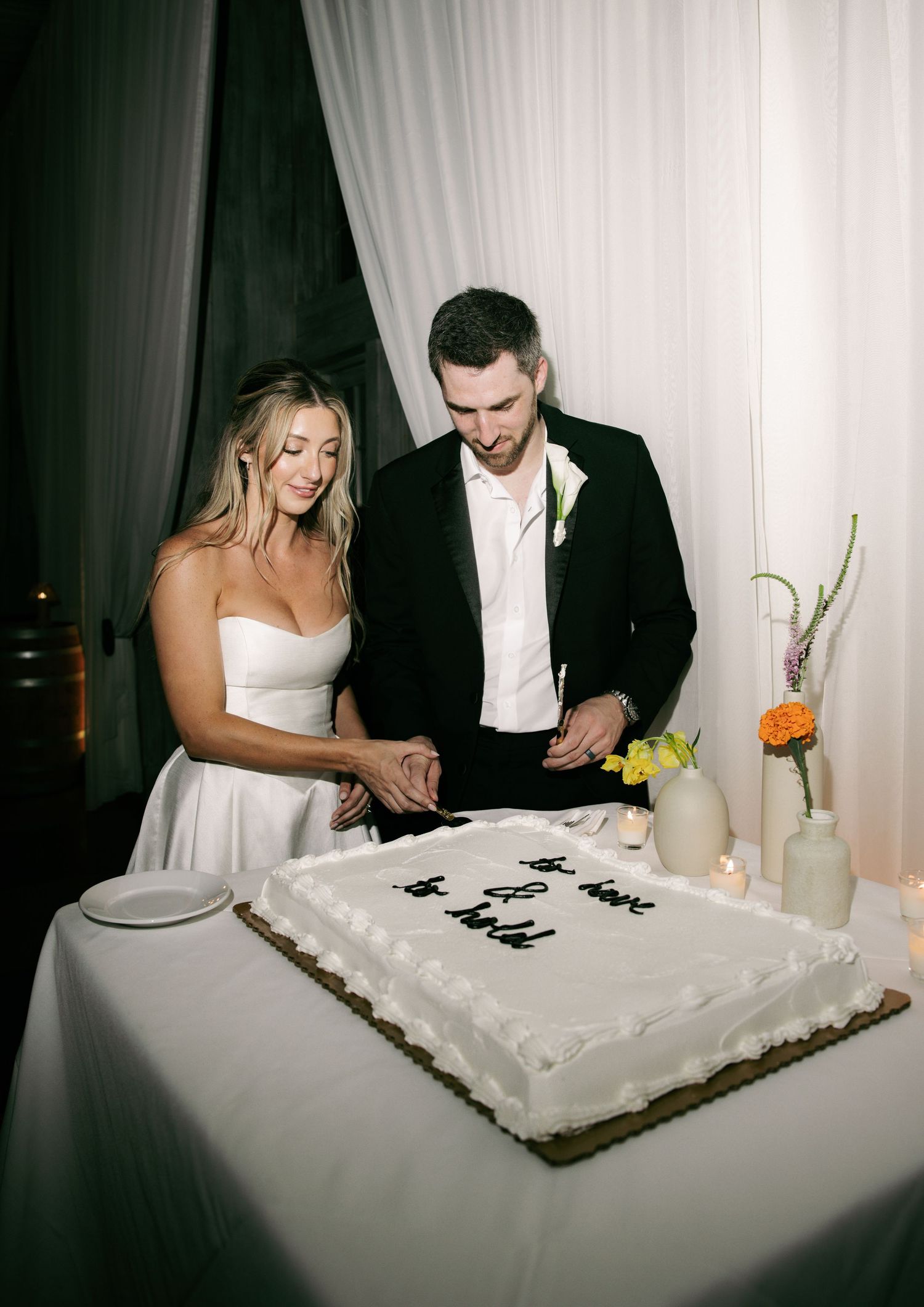 Bride and groom cutting a white sheet wedding cake with handwritten script frosting at their elegant reception.