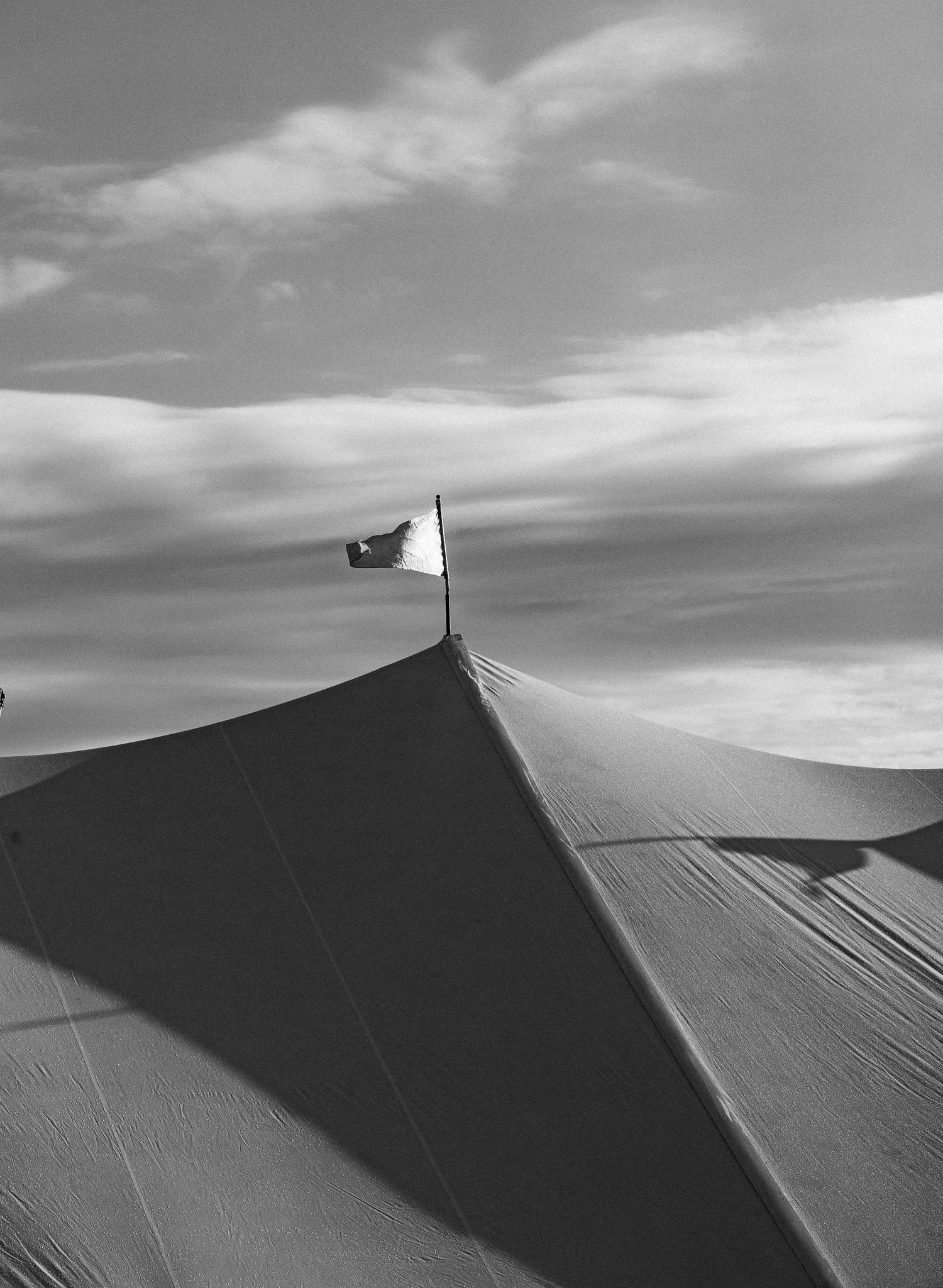 Black and white photo of a sperry tent rooftop with a flag against a dramatic cloudy sky.