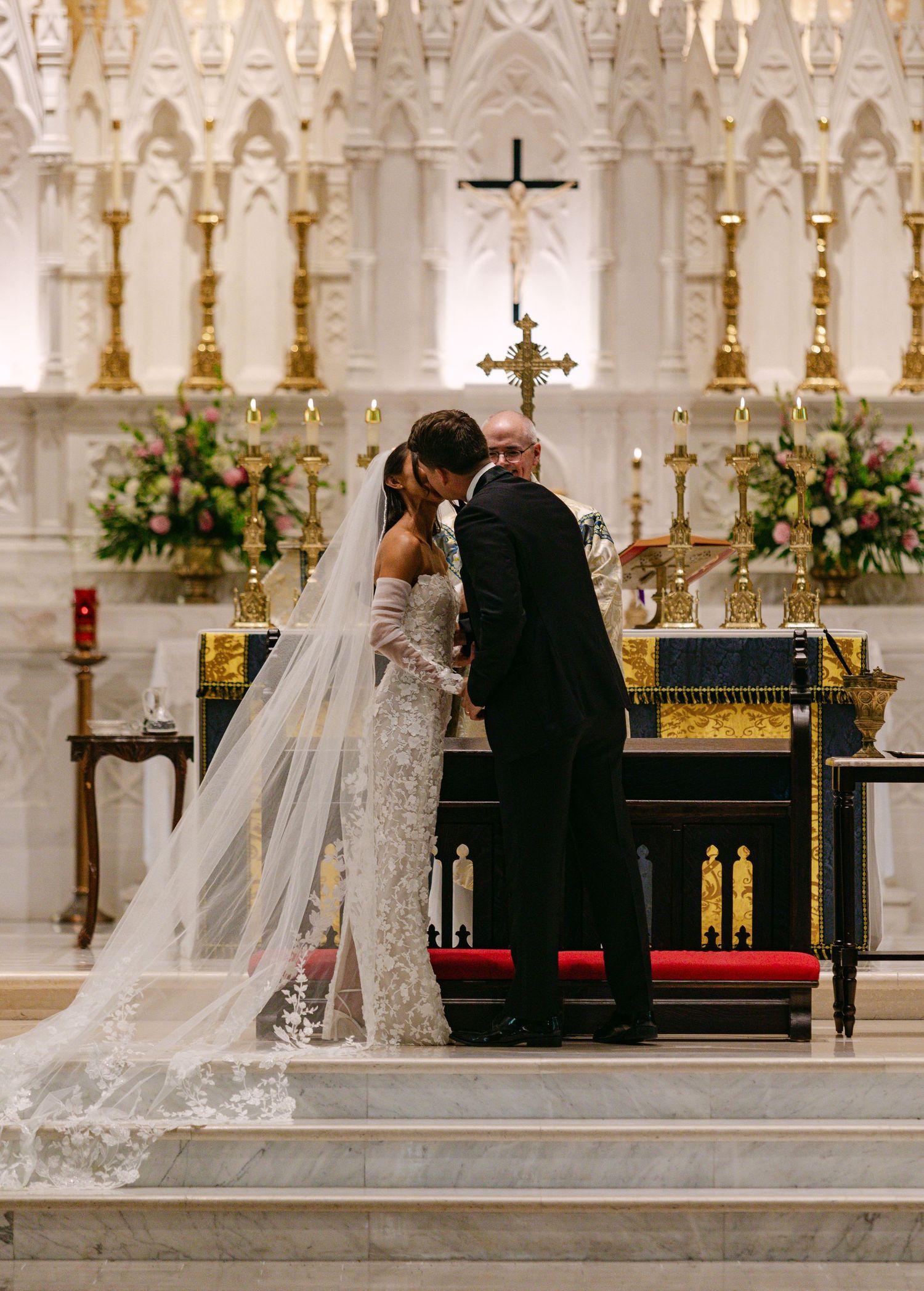 A couple stands at an ornately decorated church altar during their wedding ceremony.
