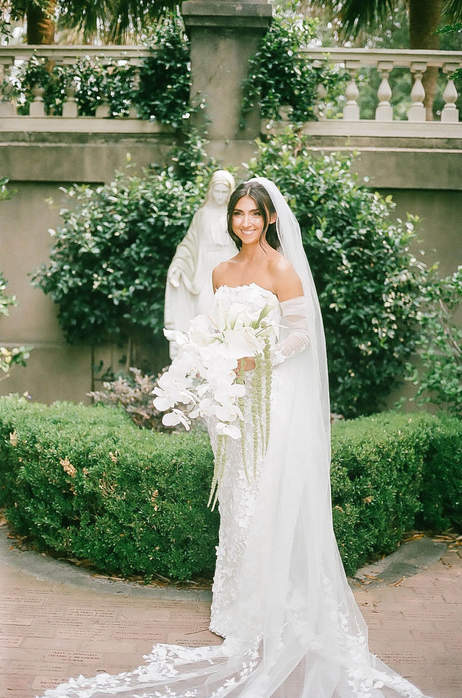 Bridal portrait in a garden setting with white orchid bouquet and flowing veil.