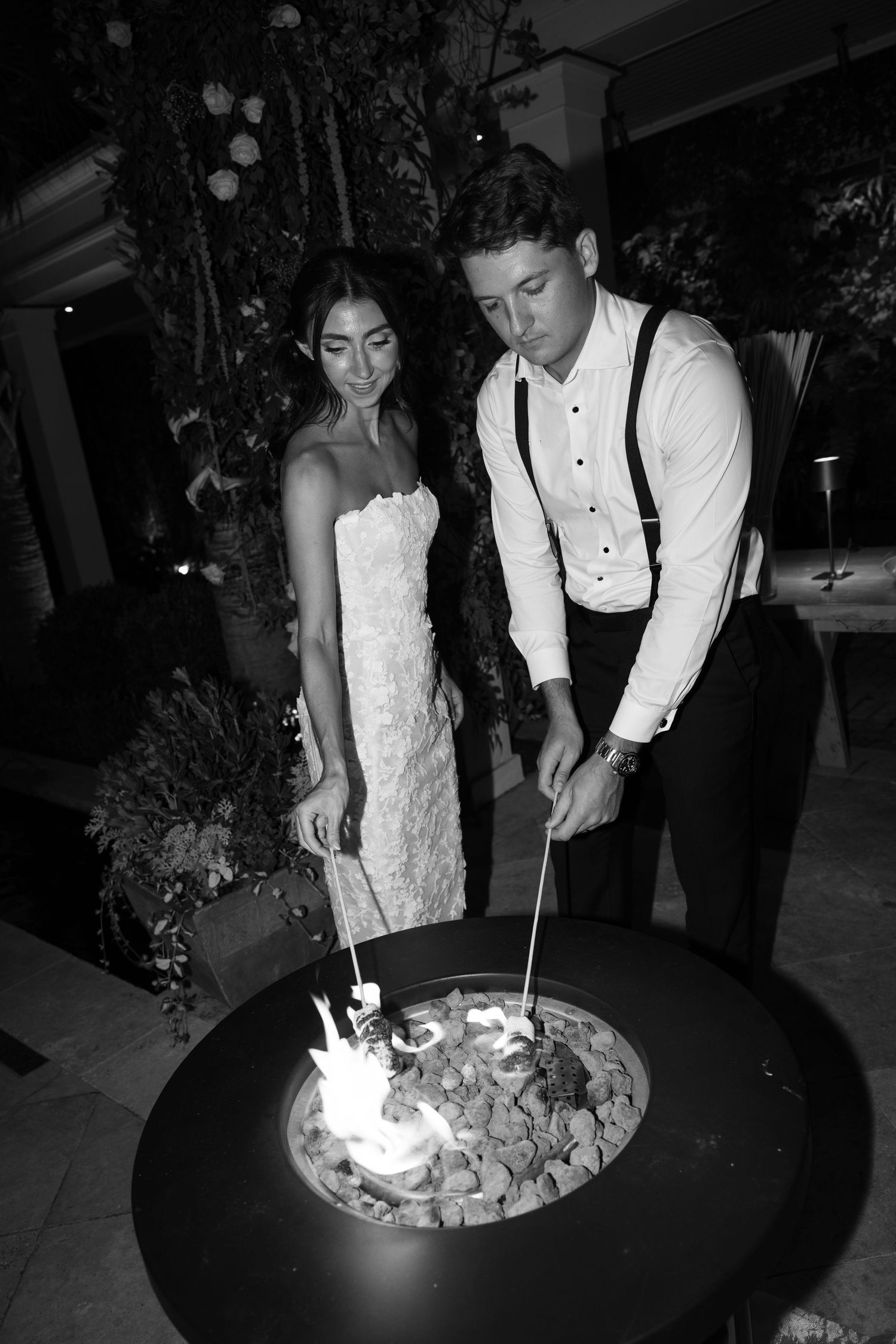 Black and white photo of couple roasting marshmallows at wedding reception.