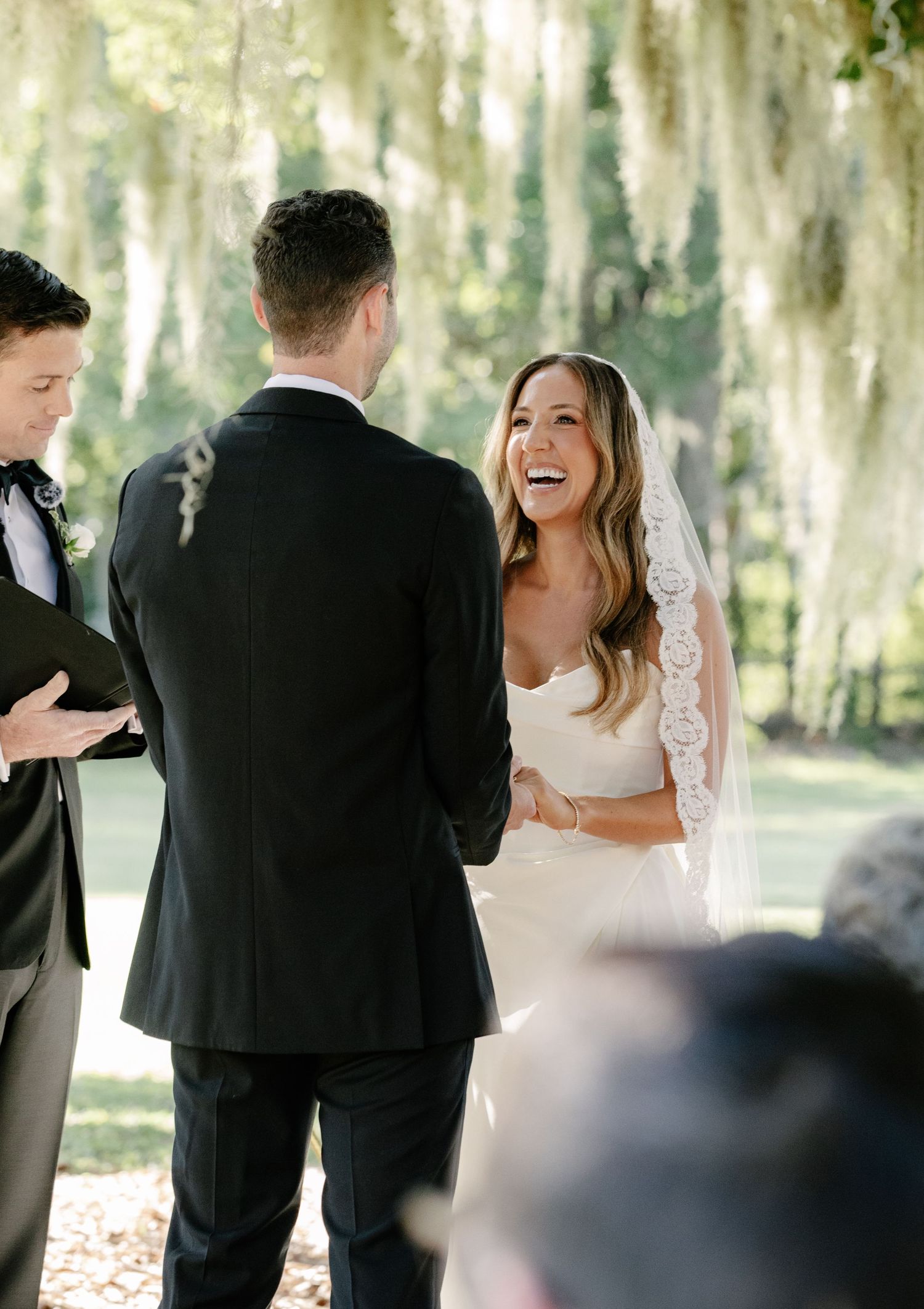 A joyful outdoor wedding ceremony moment captured in a wooded setting with Spanish moss hanging from trees.