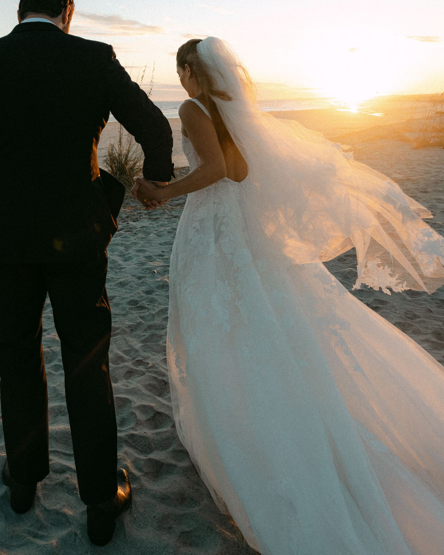A romantic beach wedding photoshoot at sunset with flowing white dress and veil catching the golden light.