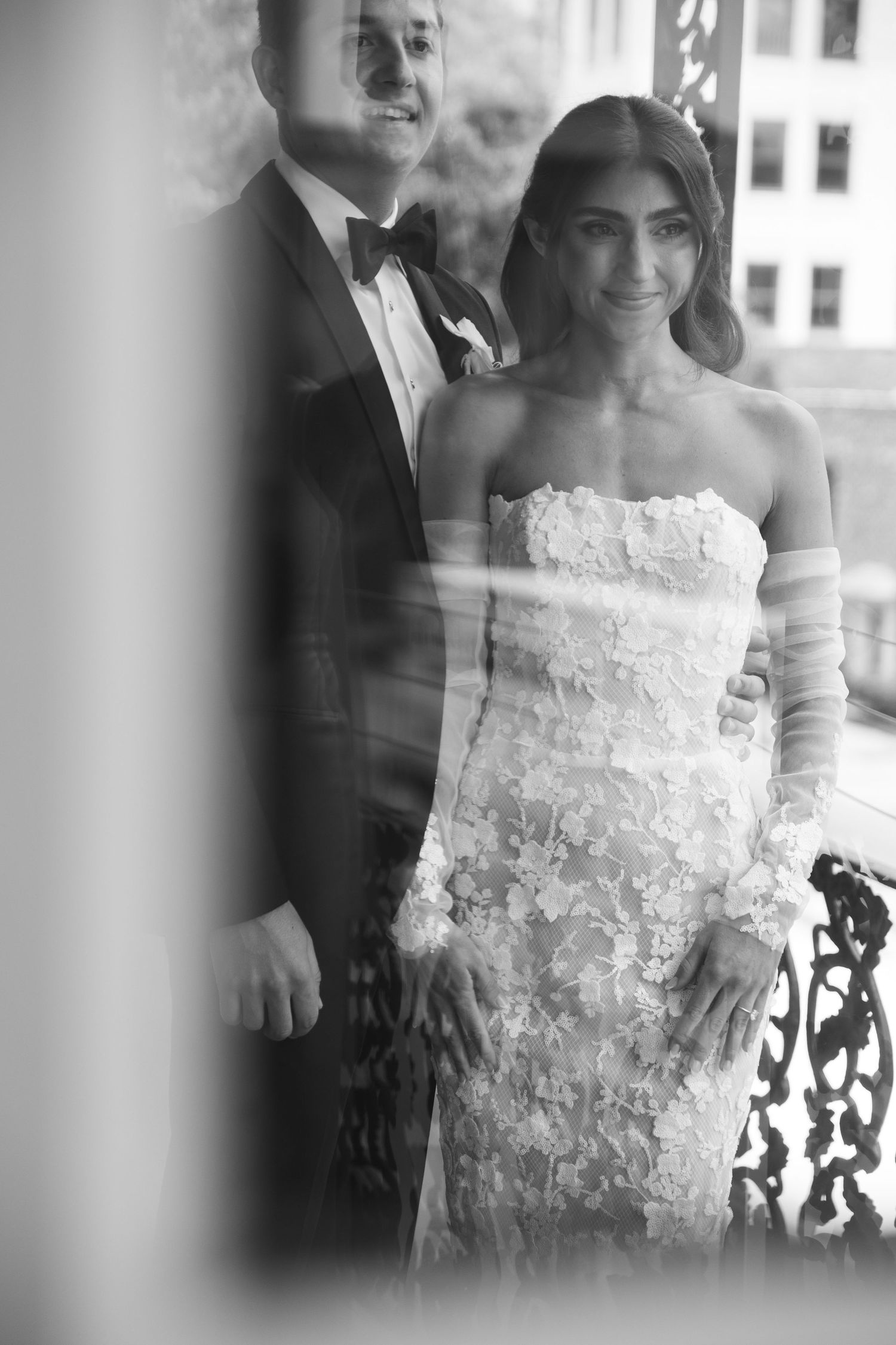 Artistic black and white portrait of newlyweds through window reflection on their wedding day.