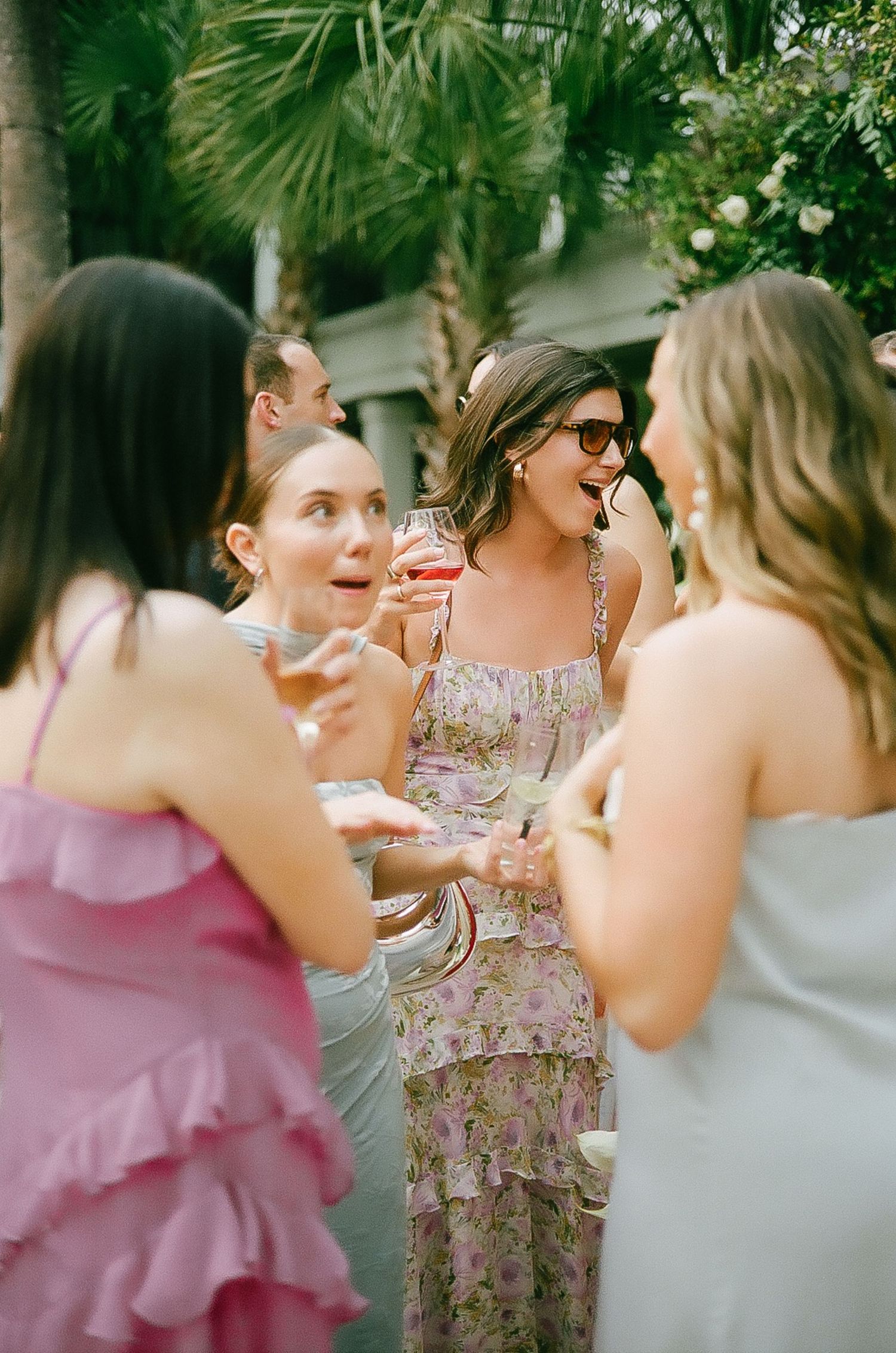 Wedding party members in pink and gray dresses chatting during an outdoor celebration.