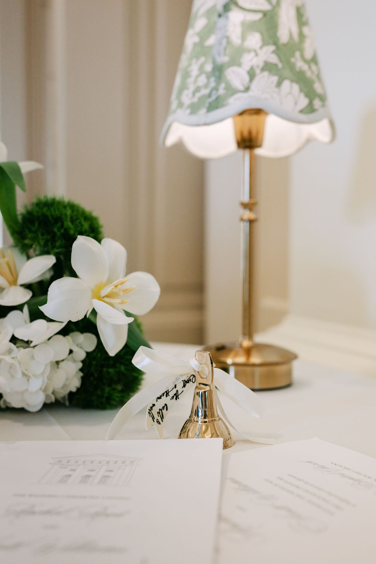 Wedding stationery and white floral bouquet with hydrangeas beside a brass lamp with green floral shade.