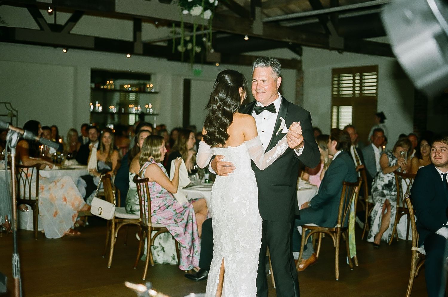 Guests dance and celebrate at an indoor wedding reception with ambient lighting.