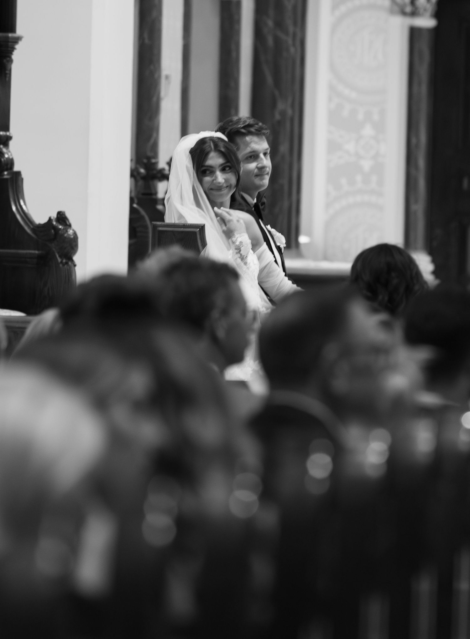 Black and white photo capturing a wedding ceremony from the perspective of church pews.