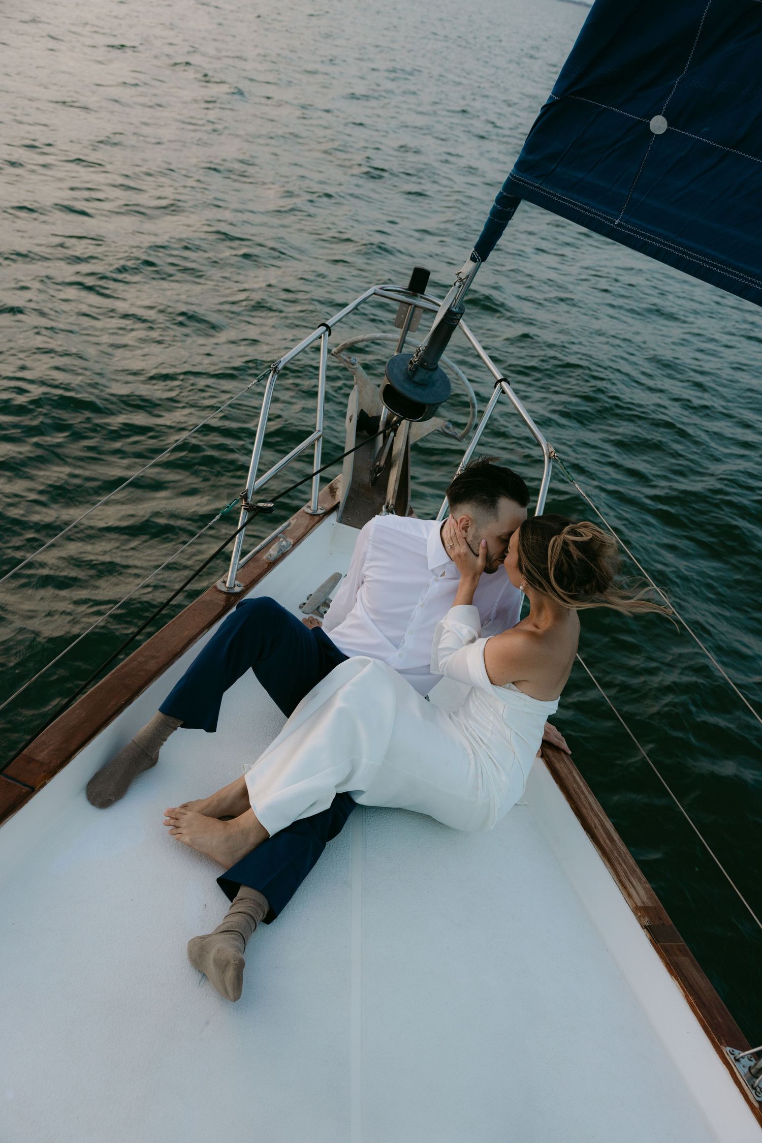 A couple relaxes on the deck of a sailboat during a romantic photoshoot at sea.