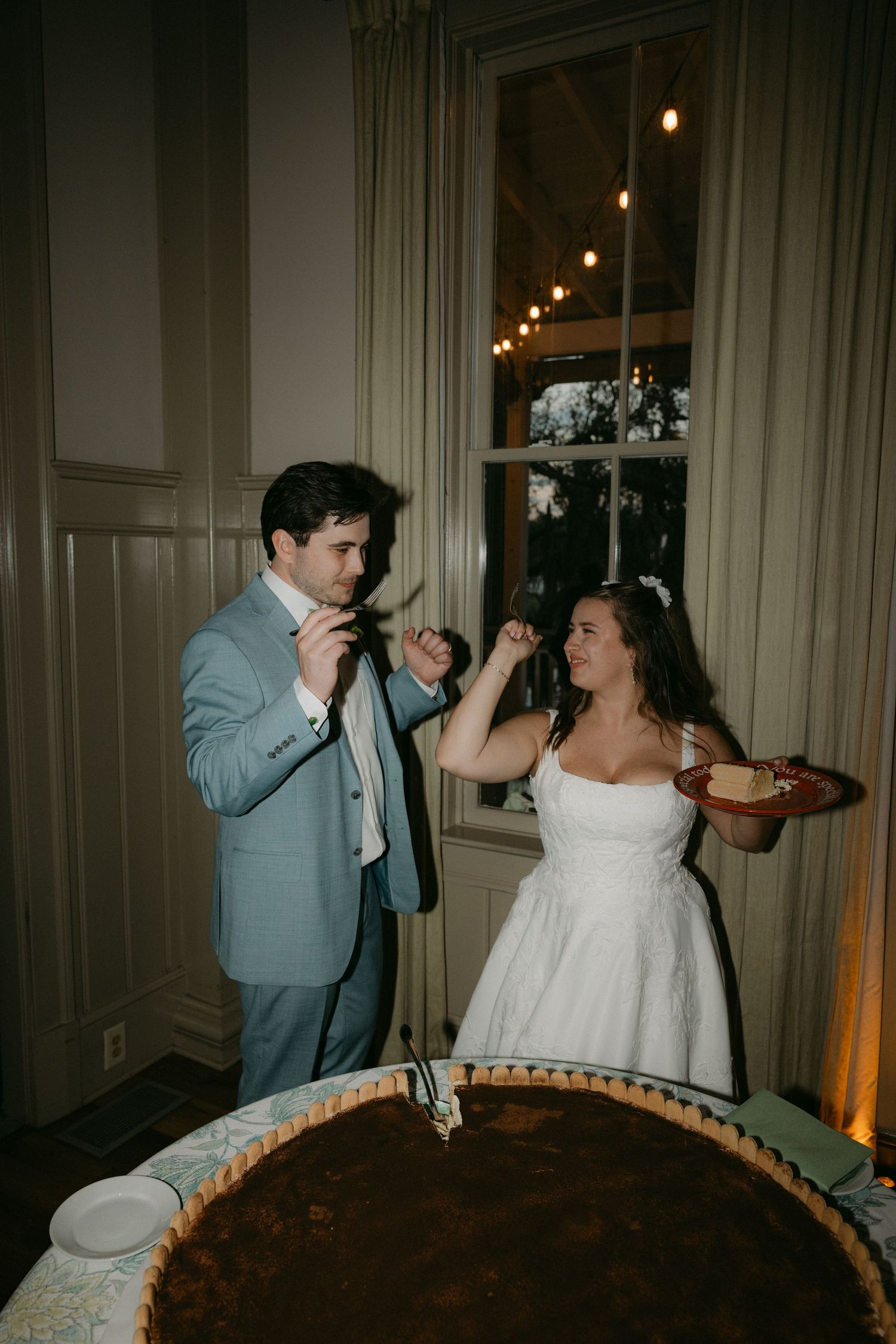 Wedding guests sharing drinks and toasting during an indoor reception with string lights.