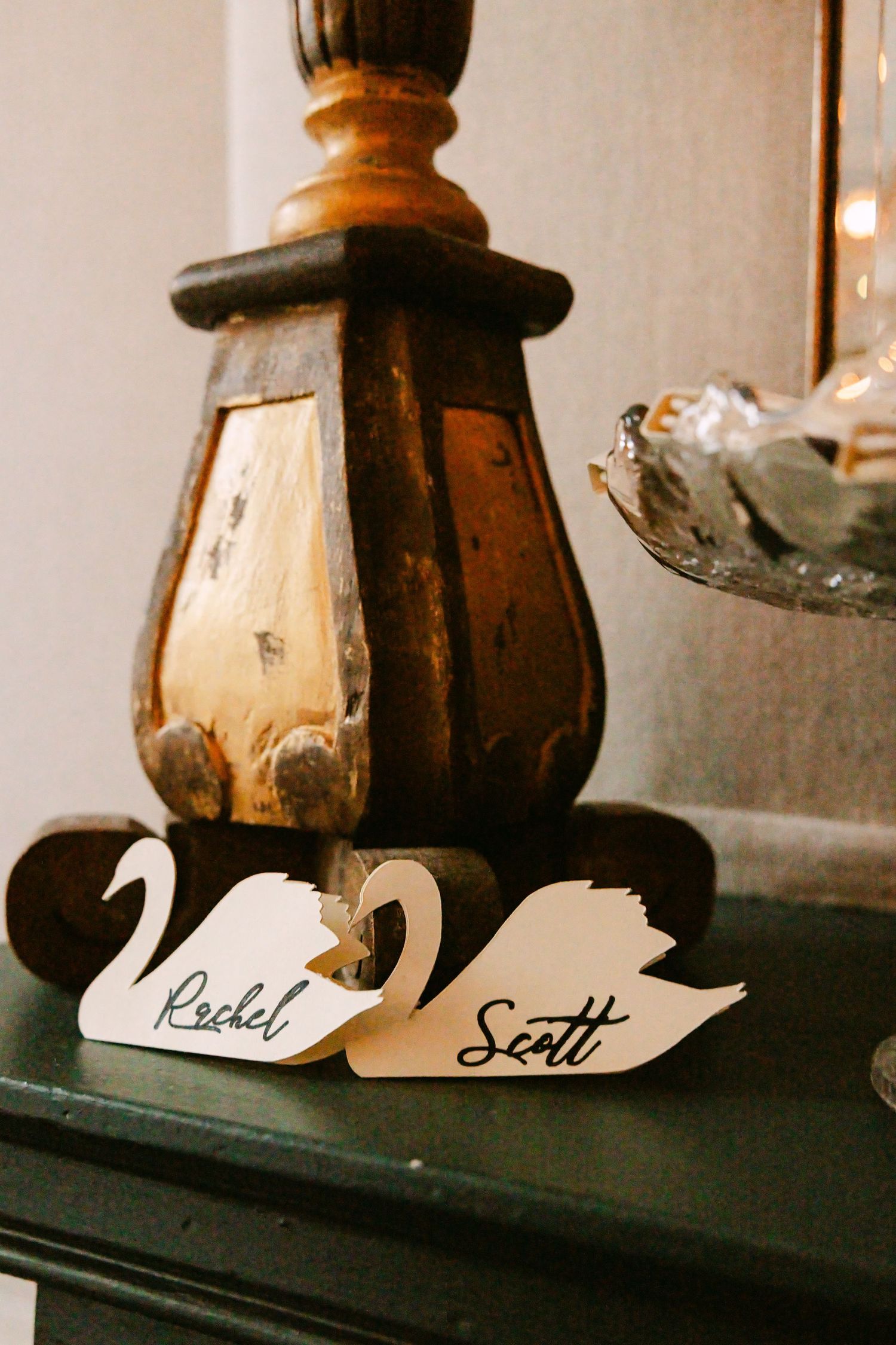 Decorative white swan-shaped place cards with names Rachel and Scott on vintage green mantelpiece.