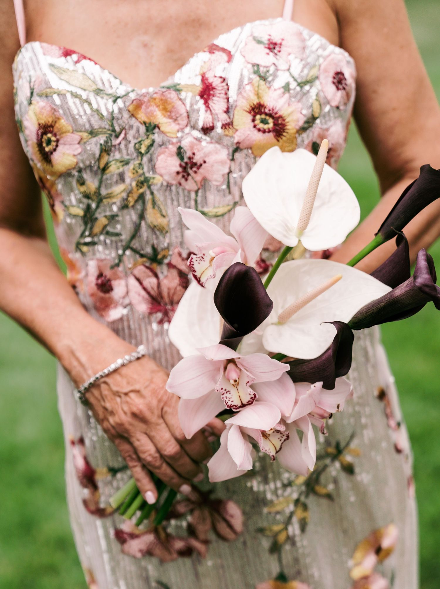 Close-up of woman holding elegant bouquet of white and dark purple calla lilies in embroidered gown.