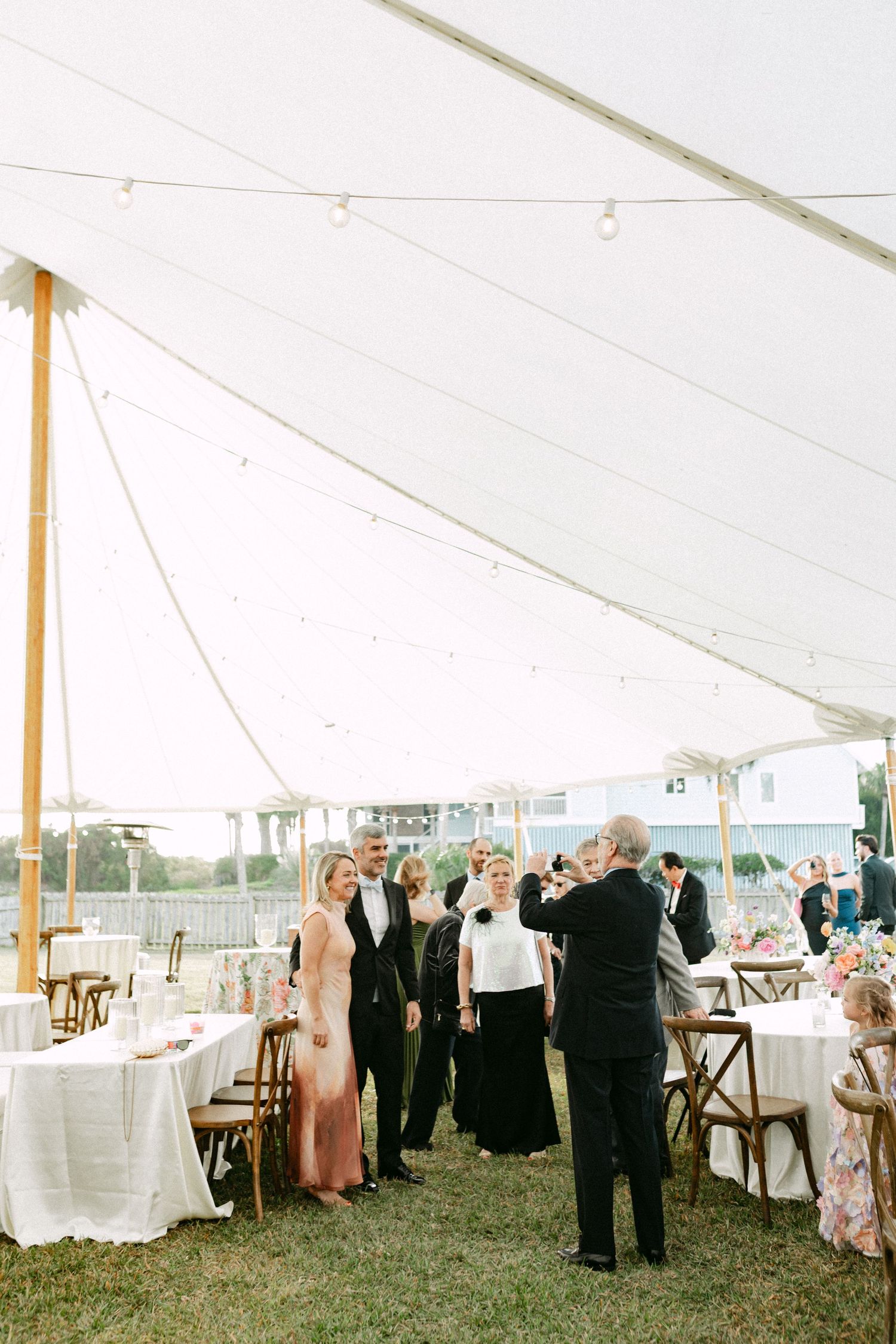 Wedding guests mingle under a white sailcloth tent with string lights at a reception.