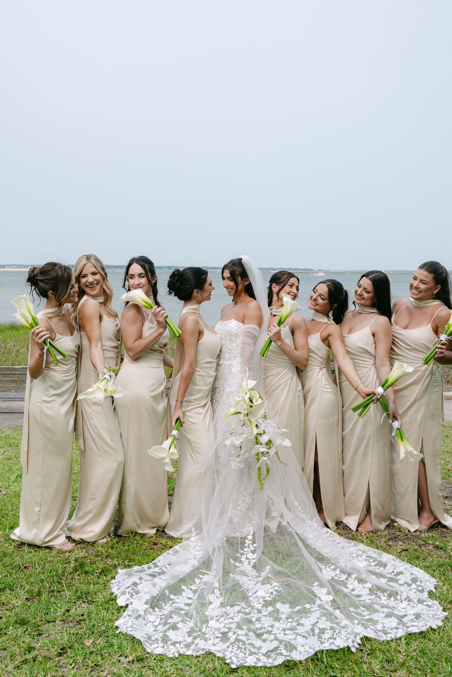 Wedding party wearing champagne dresses stands in line while holding white floral bouquets.