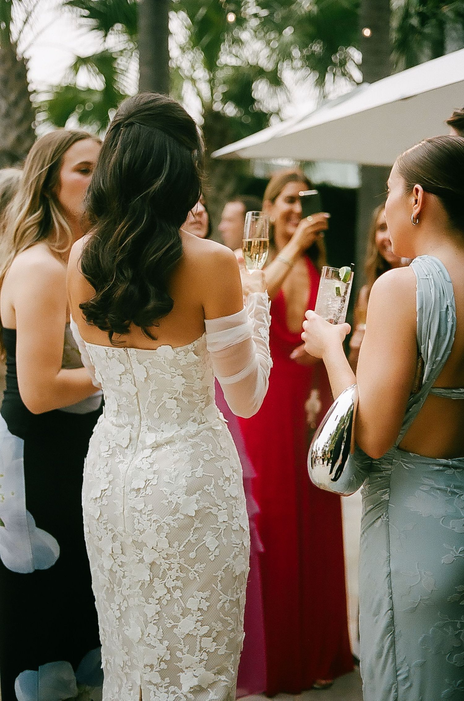 Bridesmaids in mixed color dresses celebrate with champagne at outdoor wedding reception.