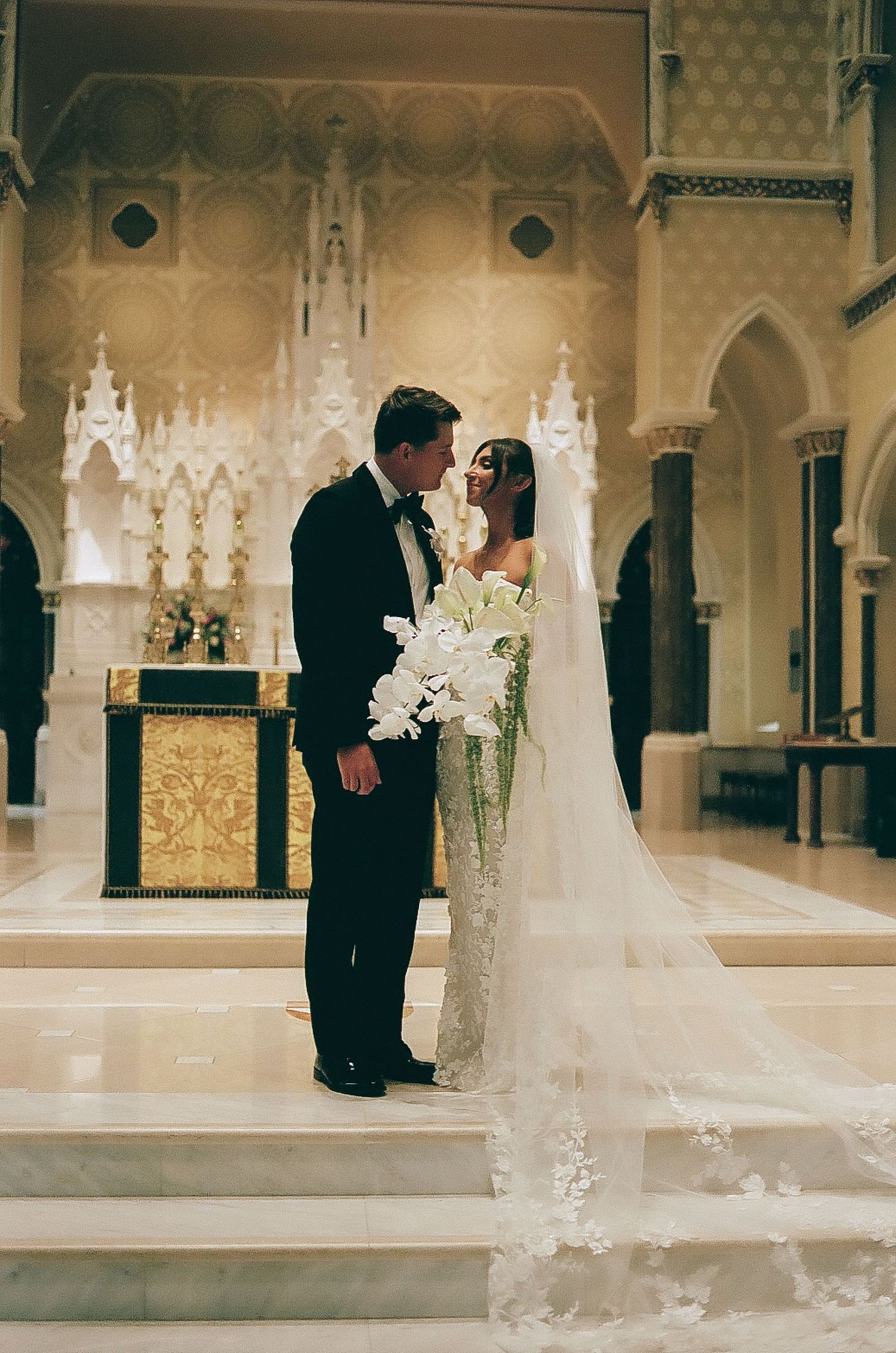 Elegant wedding couple shares intimate moments in a grand ornate hall with gothic architecture.