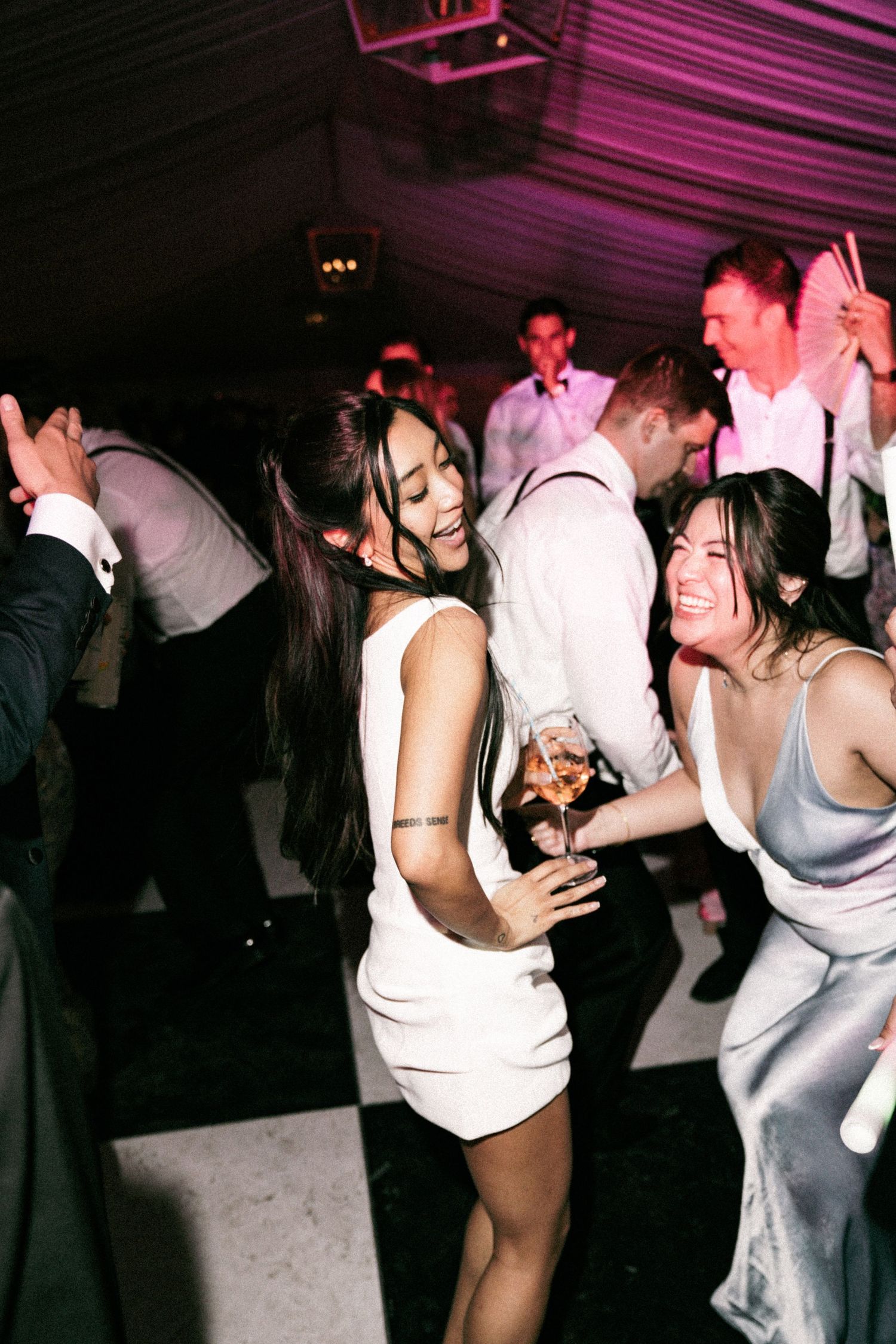 Bride in white mini dress dancing joyfully with guests at lively wedding reception.