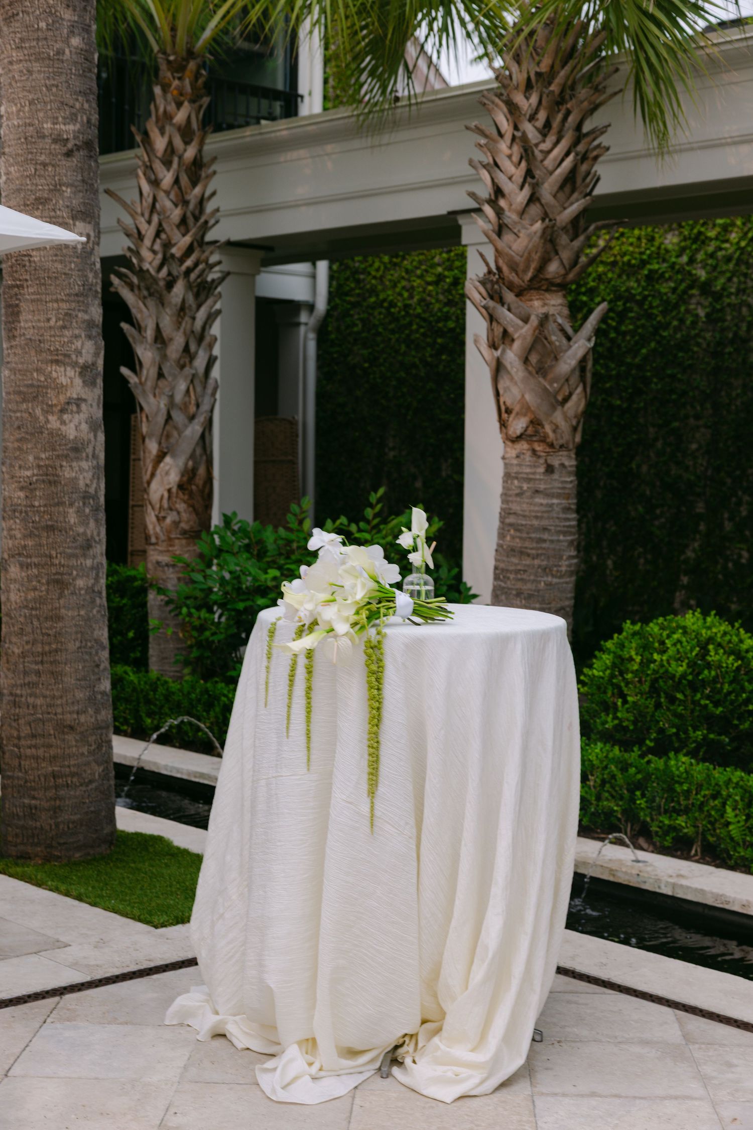 White-clothed round tables set up on an elegant patio surrounded by palm trees.