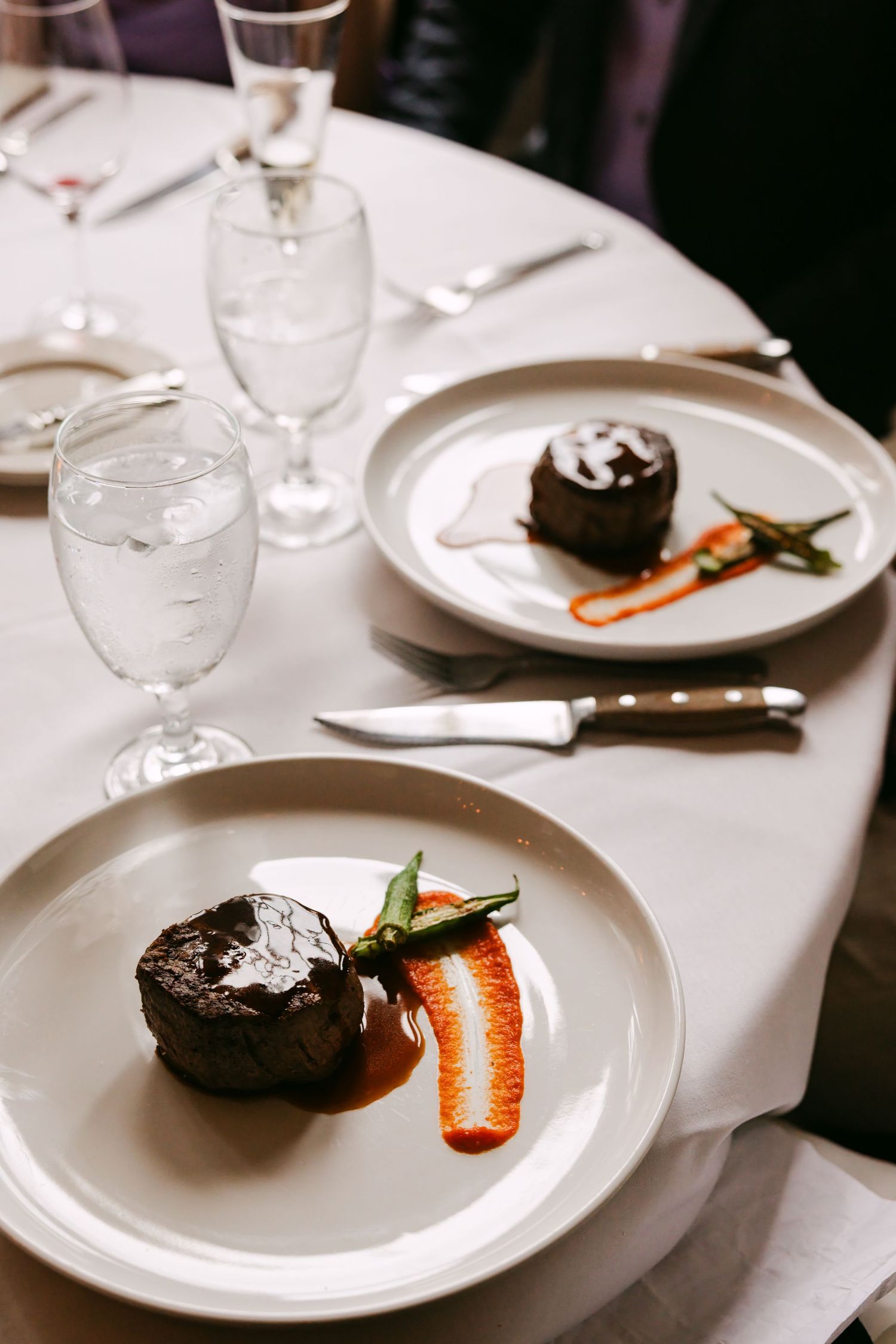 Elegant wedding reception dinner plates featuring filet mignon with red pepper coulis and green beans on white linens.