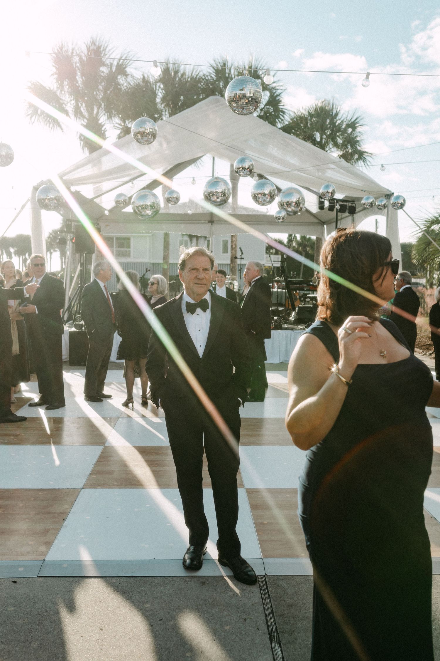 Elegant outdoor wedding reception with disco balls under a white canopy, guests in formal attire on a dance floor.