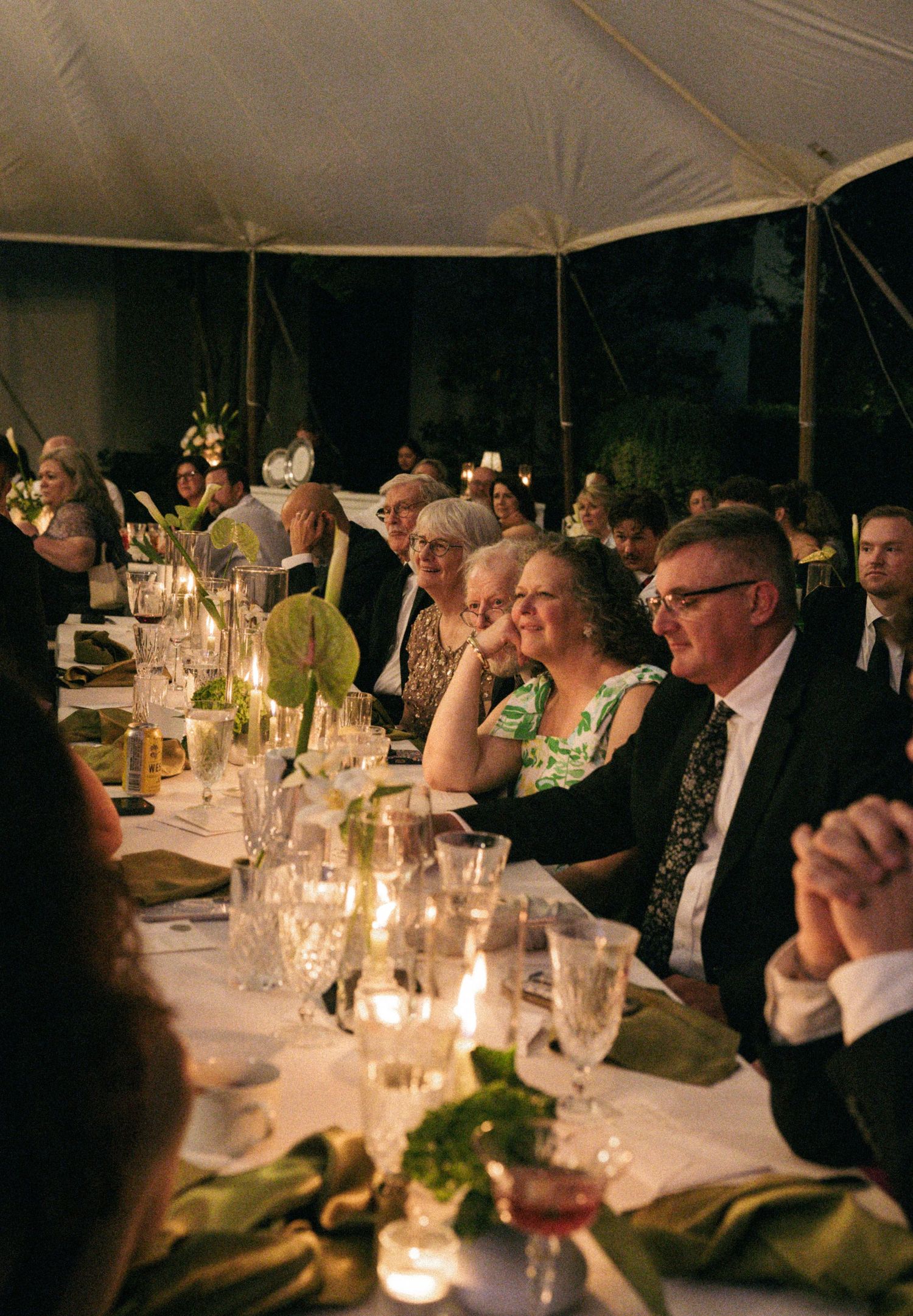 Wedding guests seated at candlelit reception tables under tent during elegant evening dinner.