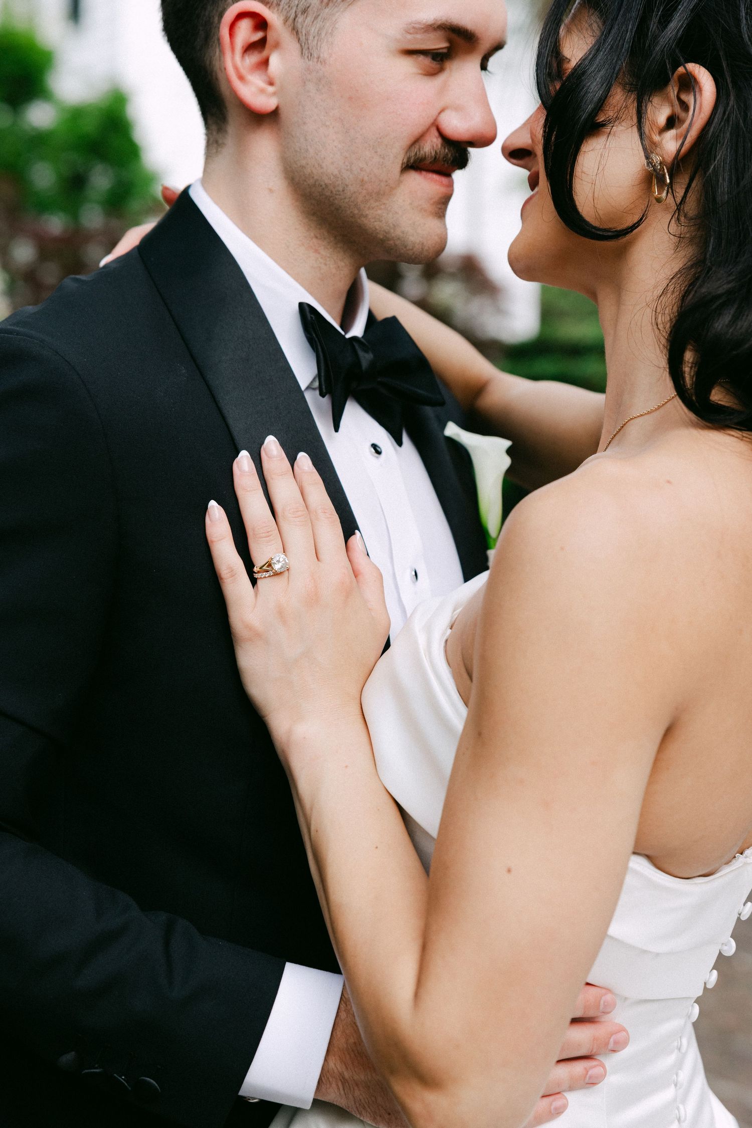 Bride and groom share an intimate moment, with bride in strapless white gown and groom in black tuxedo with bow tie.