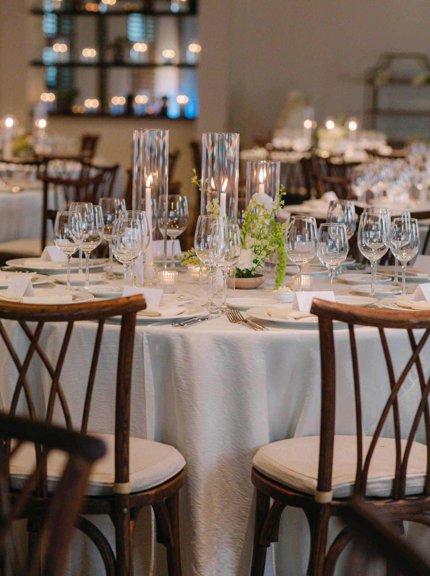 Formal dining table set with white linens, wine glasses and crossback chairs for wedding reception.