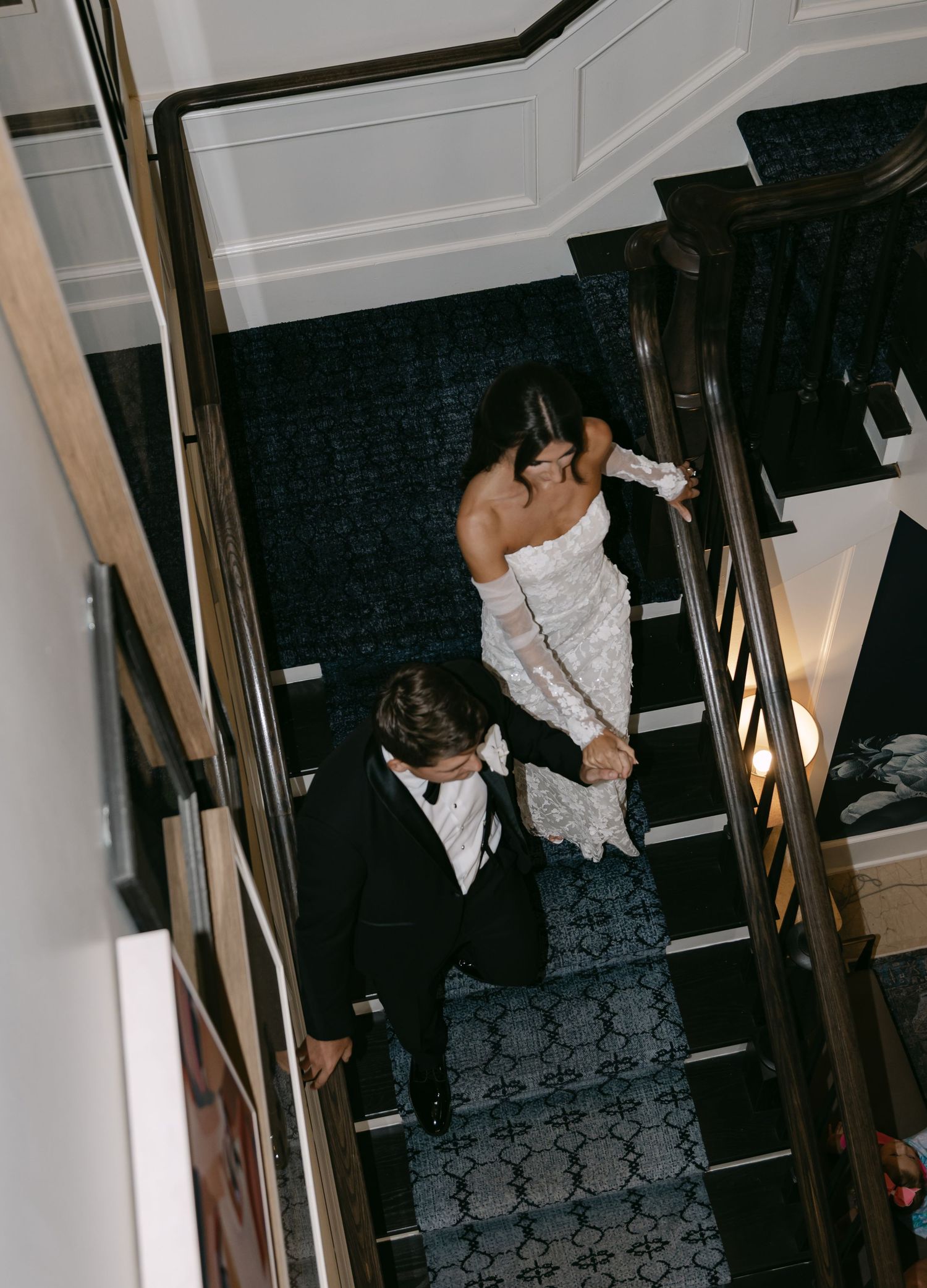 Bride and groom descend a carpeted staircase during their wedding day.