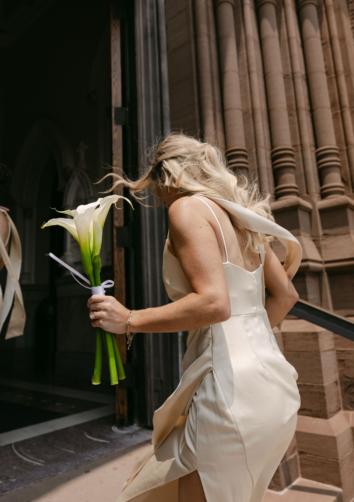 A bridal bouquet with white lilies is held against an architectural background.
