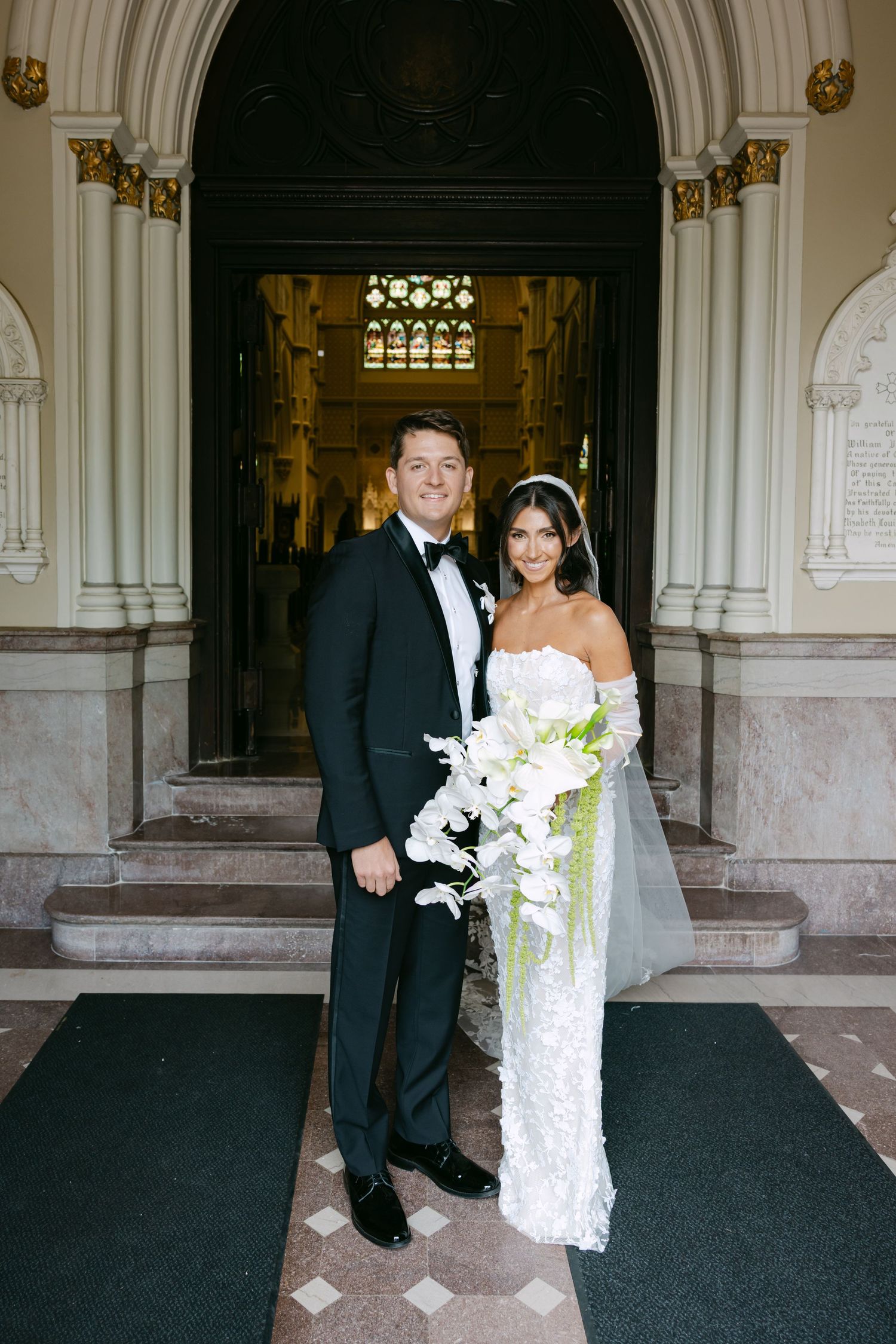 Wedding couple poses under arched church entrance with ornate architectural details.