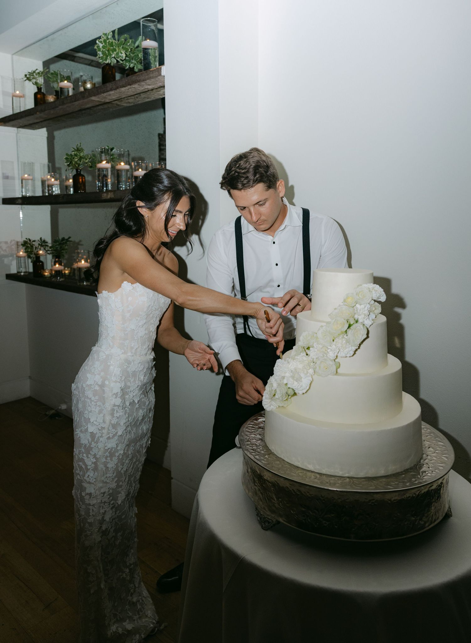 Newlyweds sharing a playful moment while cutting their elegant white wedding cake.