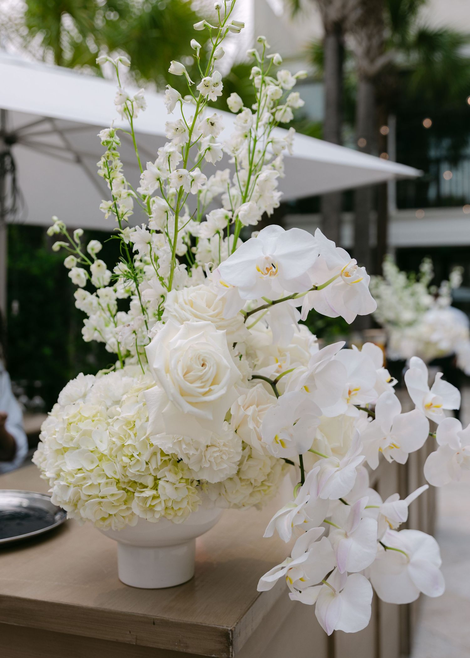 Elegant white floral arrangement with roses, orchids and hydrangeas in modern vase.