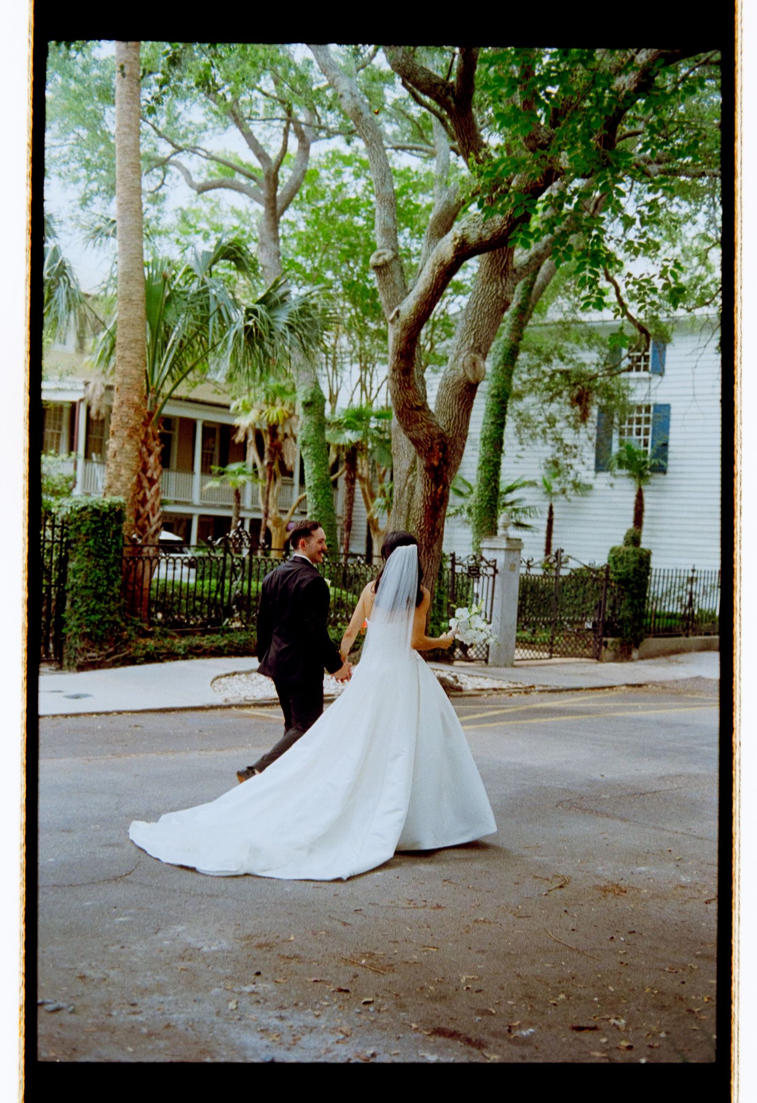 Bride and groom walk hand in hand on a tree-lined street after wedding.