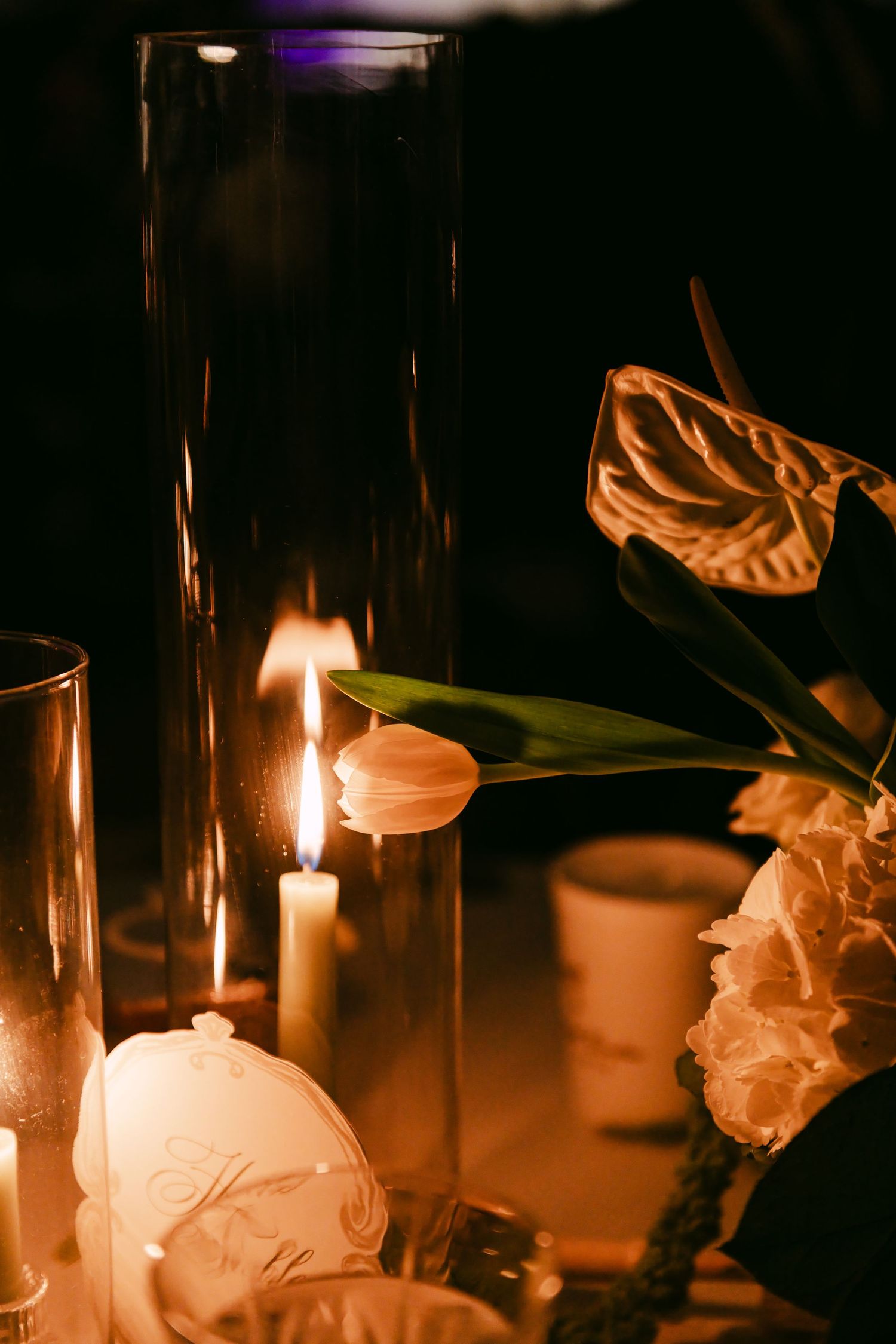 Romantic candlelit wedding table with tulips and anthurium flowers in warm amber light.