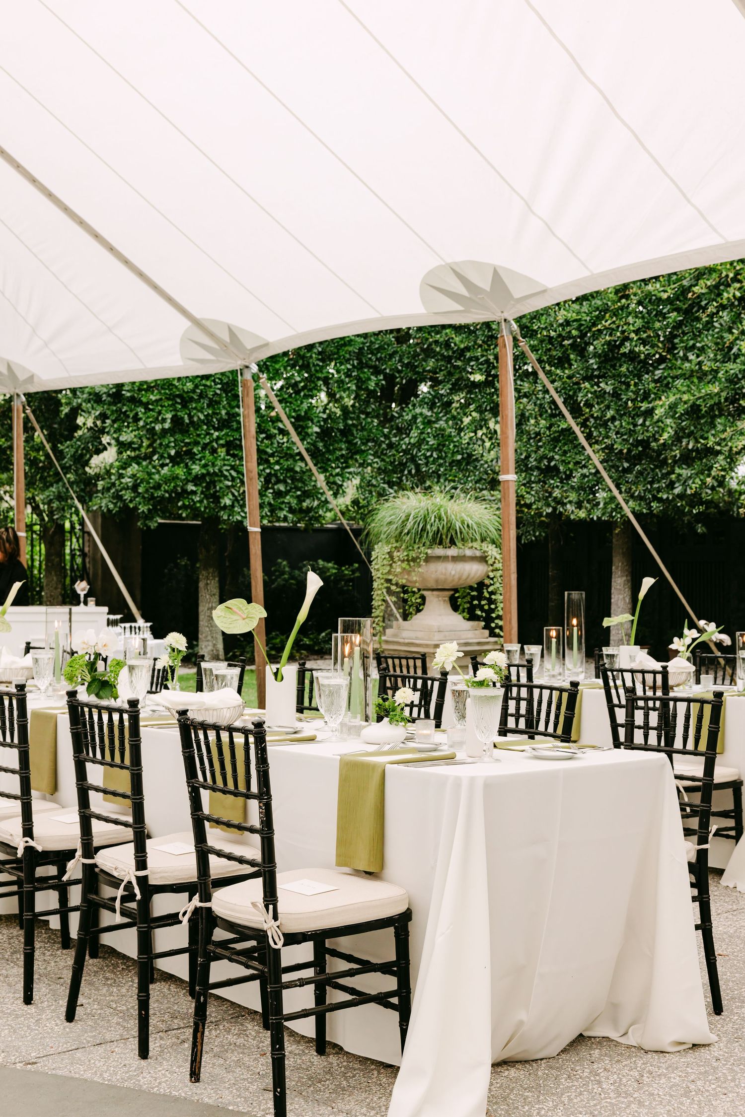 Elegant outdoor wedding reception under white tent with black chiavari chairs and green floral centerpieces.