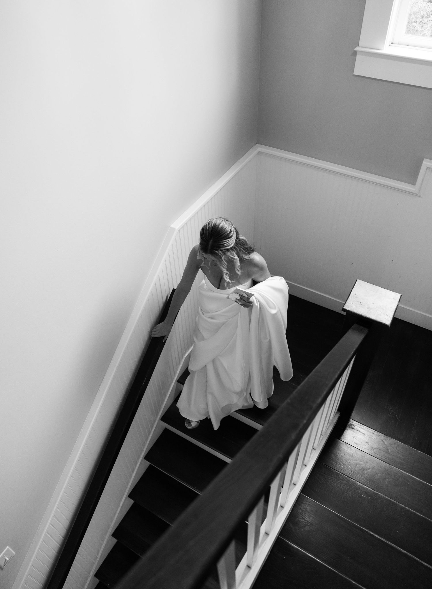 Black and white aerial view of bride in wedding gown descending elegant staircase.