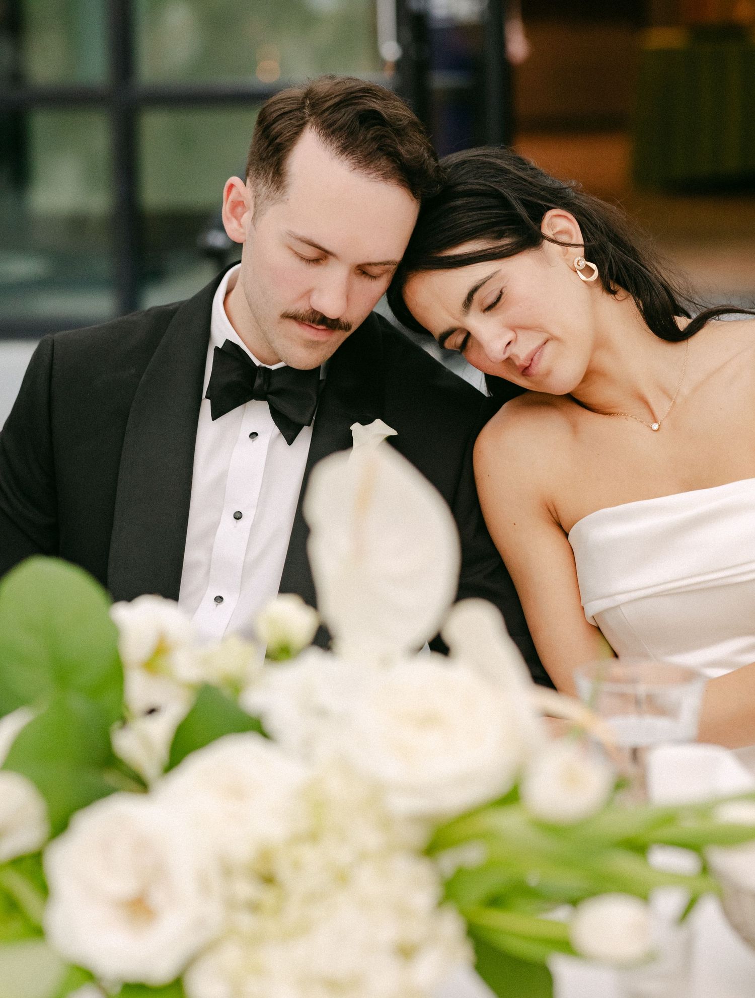 Bride and groom share intimate moment at wedding reception table adorned with white floral centerpieces.