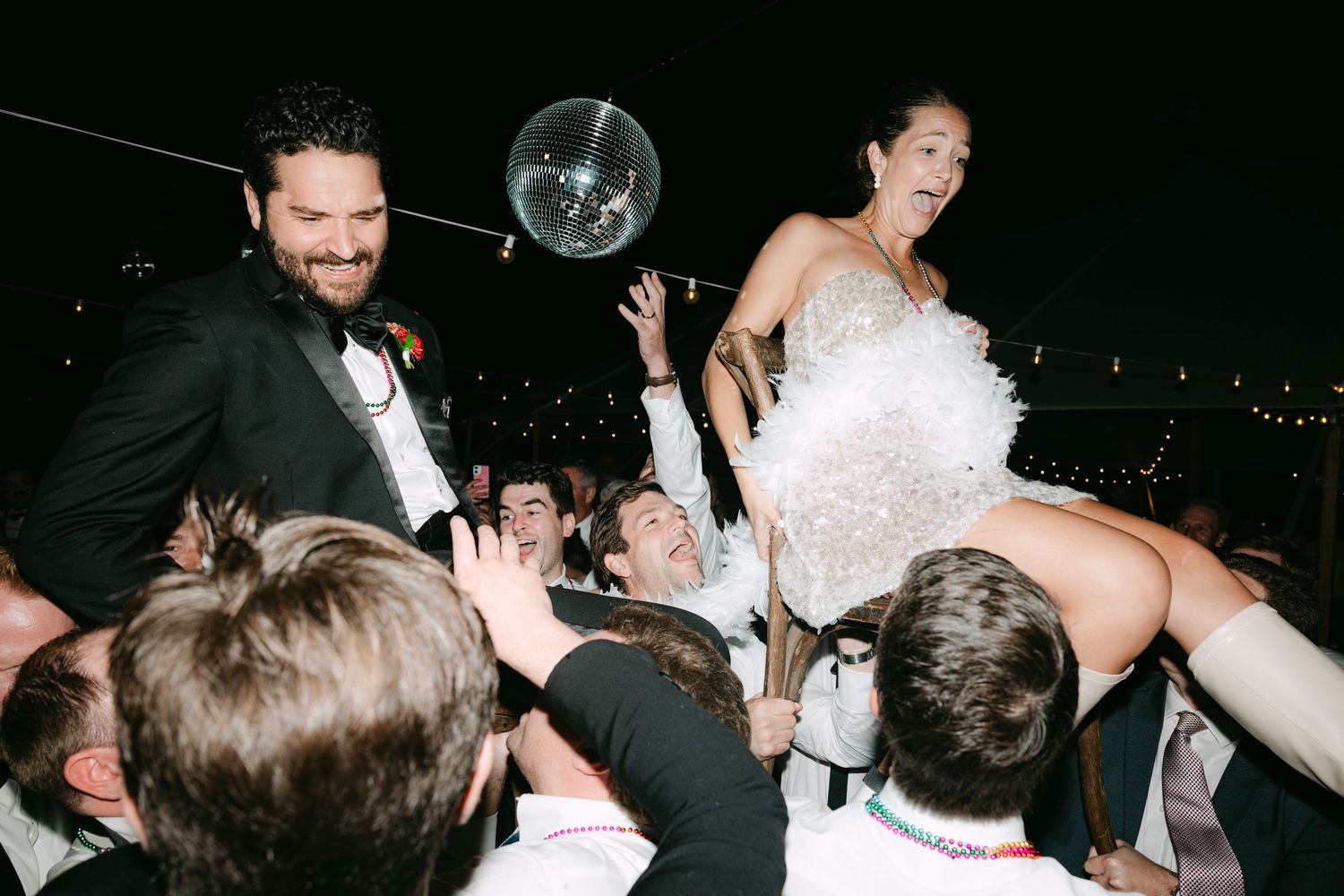Joyful bride lifted by guests on the dance floor at lively wedding reception celebration.