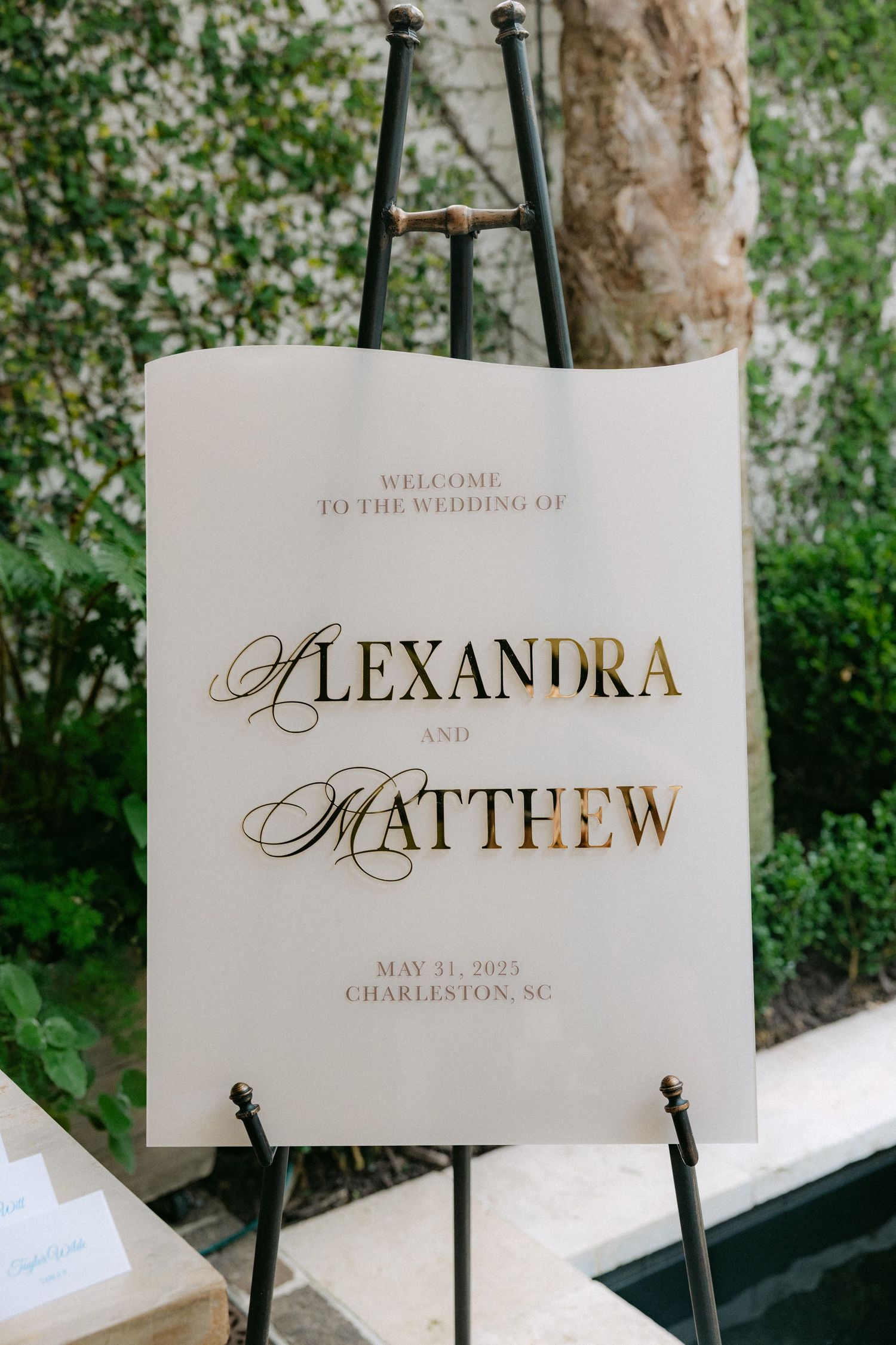 Elegant wedding welcome sign displaying names in gold calligraphy on white paper.