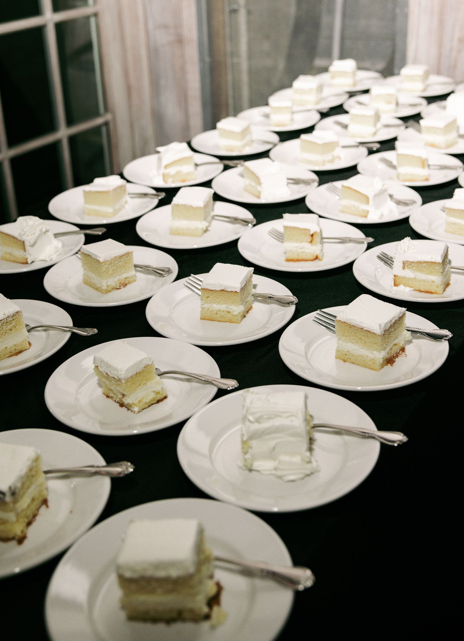 Rows of white plates with slices of white wedding cake and silver forks ready for guests.