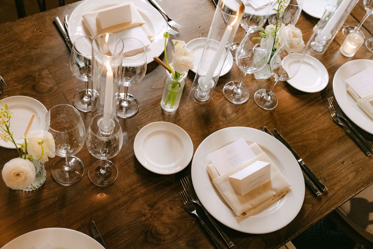 Overhead view of formal table settings with white plates and glassware on a dark wooden surface.