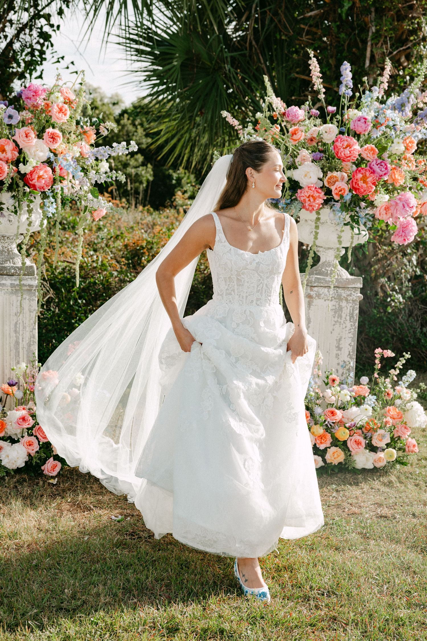 Bride twirls in a lace wedding gown before a colorful floral arch outdoors.