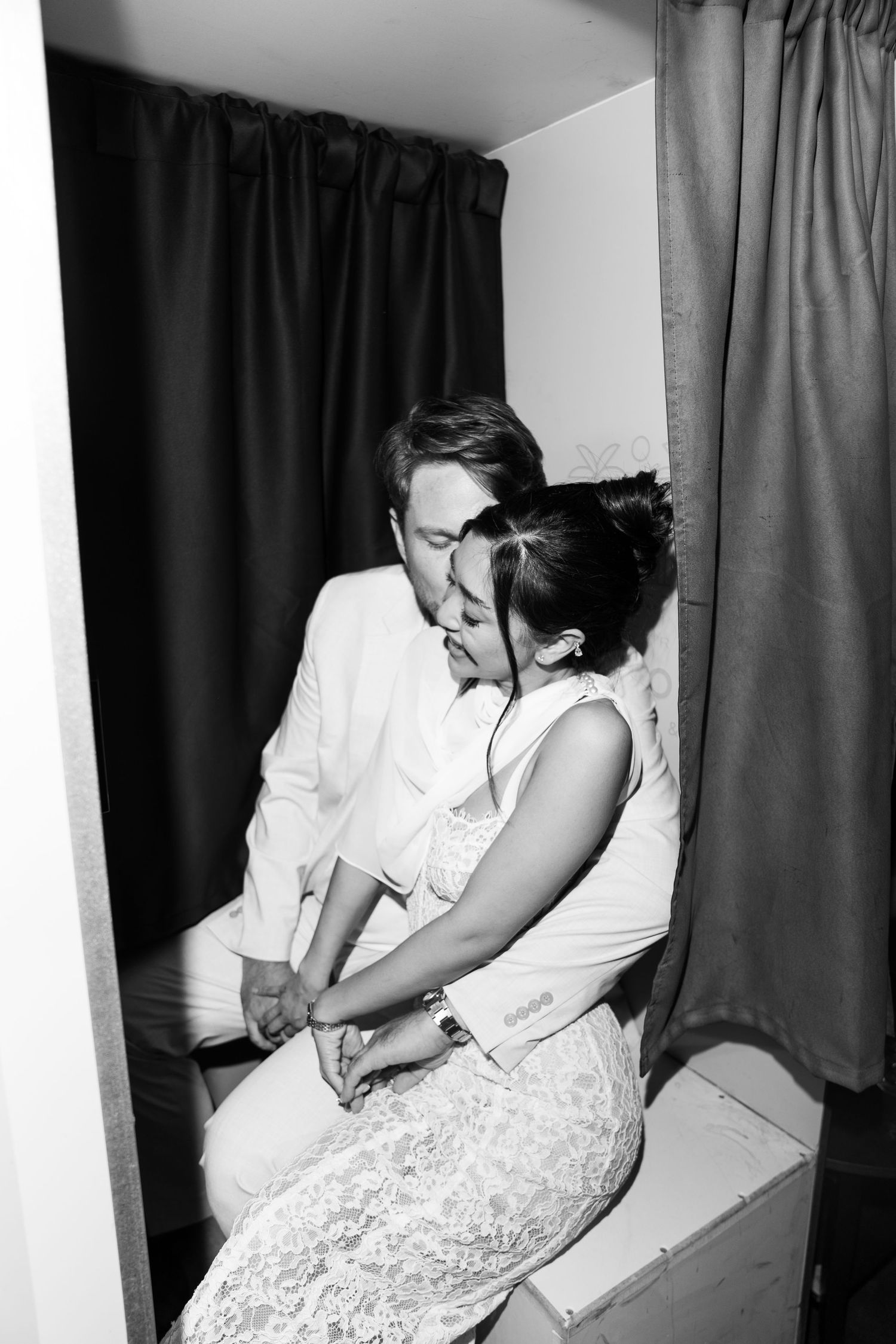 Black and white photo of a romantic couple sharing a tender moment in a photo booth on their wedding day.
