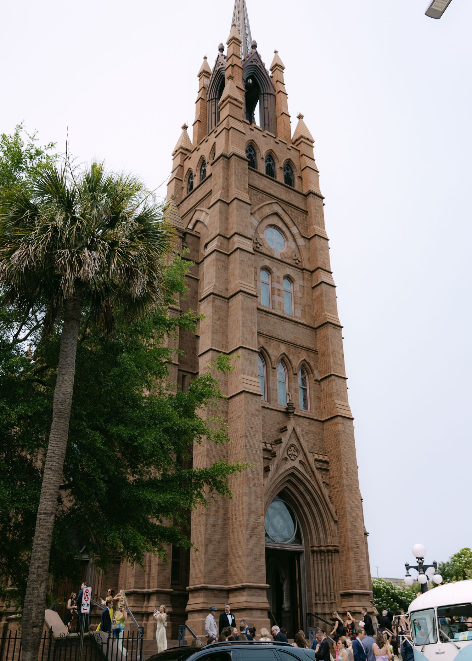 Gothic cathedral exterior with palm trees and stone spires reaching into cloudy sky.
