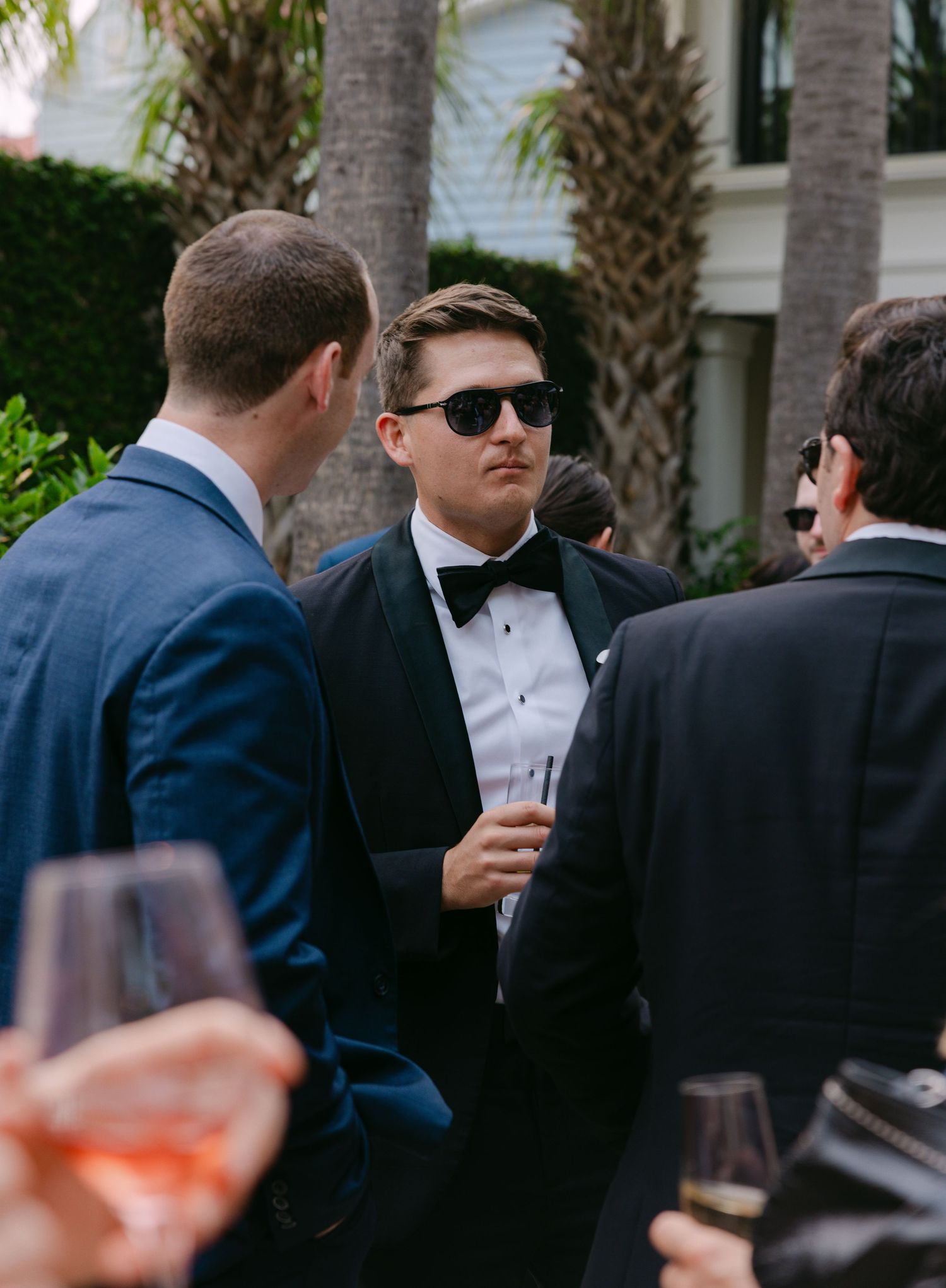 Well-dressed guests in formal attire socialize at an outdoor wedding reception.