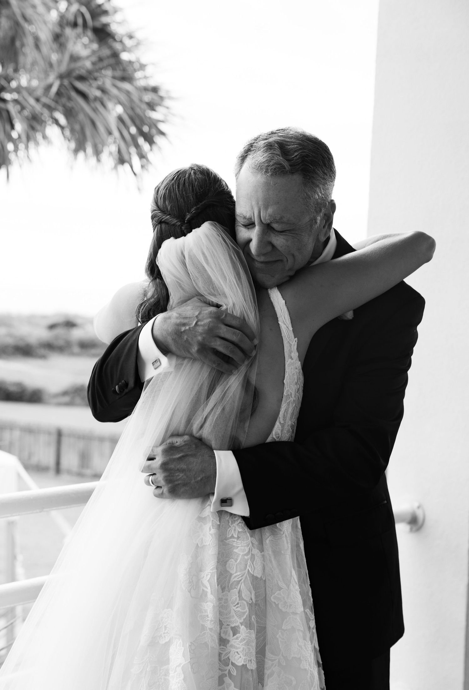 Emotional father hugging his daughter in a wedding dress in a black and white photo.