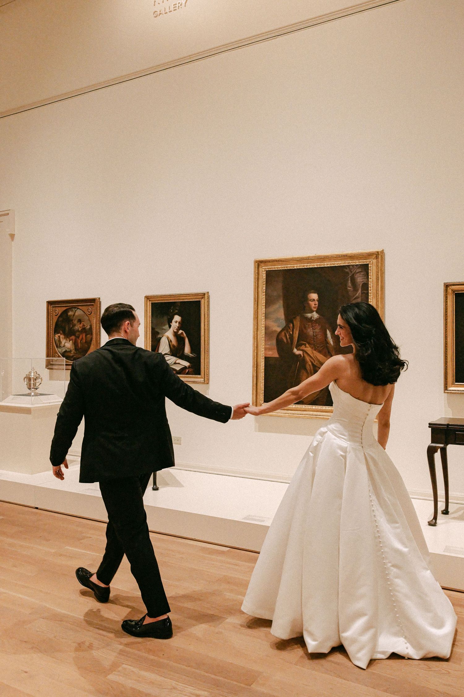 Bride and groom holding hands walking through art museum gallery on their wedding day.